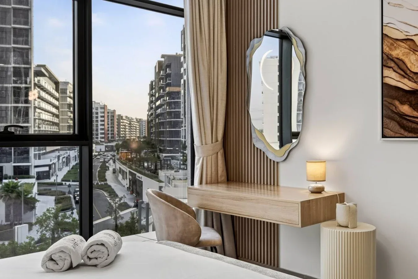 A bedroom with a large window overlooking a city street.