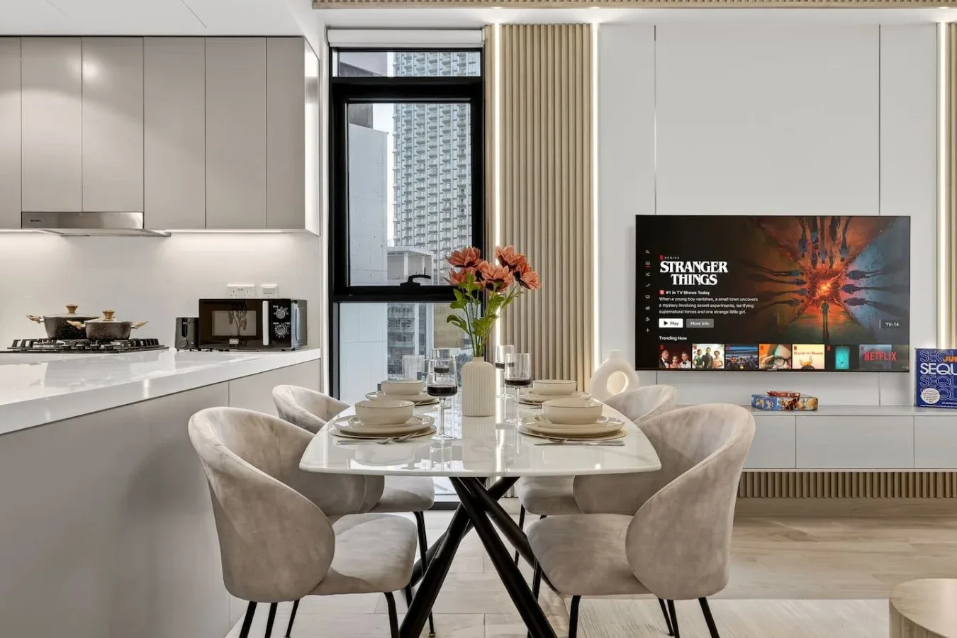 A modern dining area with a set table beside an open kitchen and wall-mounted television.