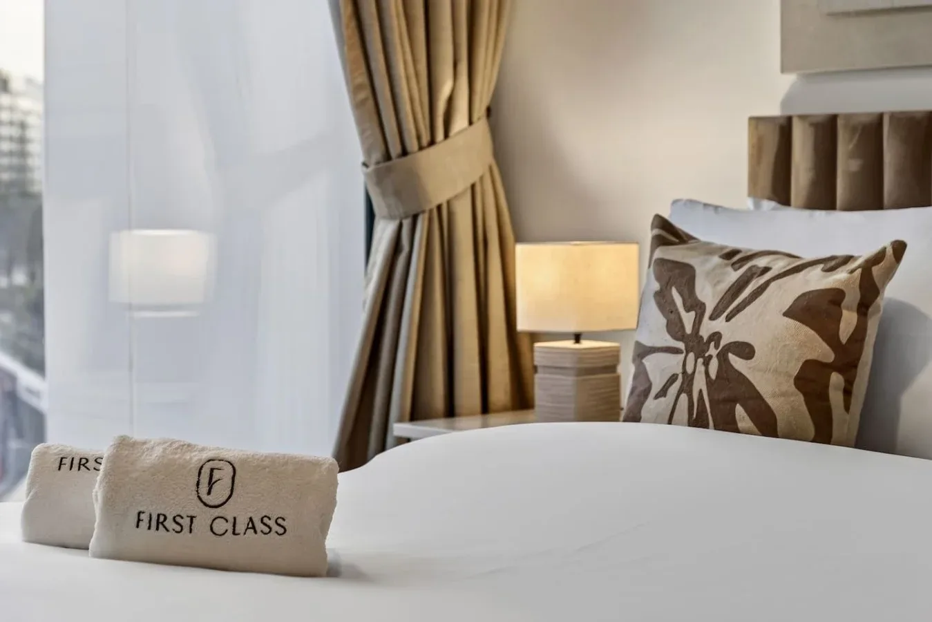 A bedroom with a neatly made bed, patterned pillows, and a bedside lamp.