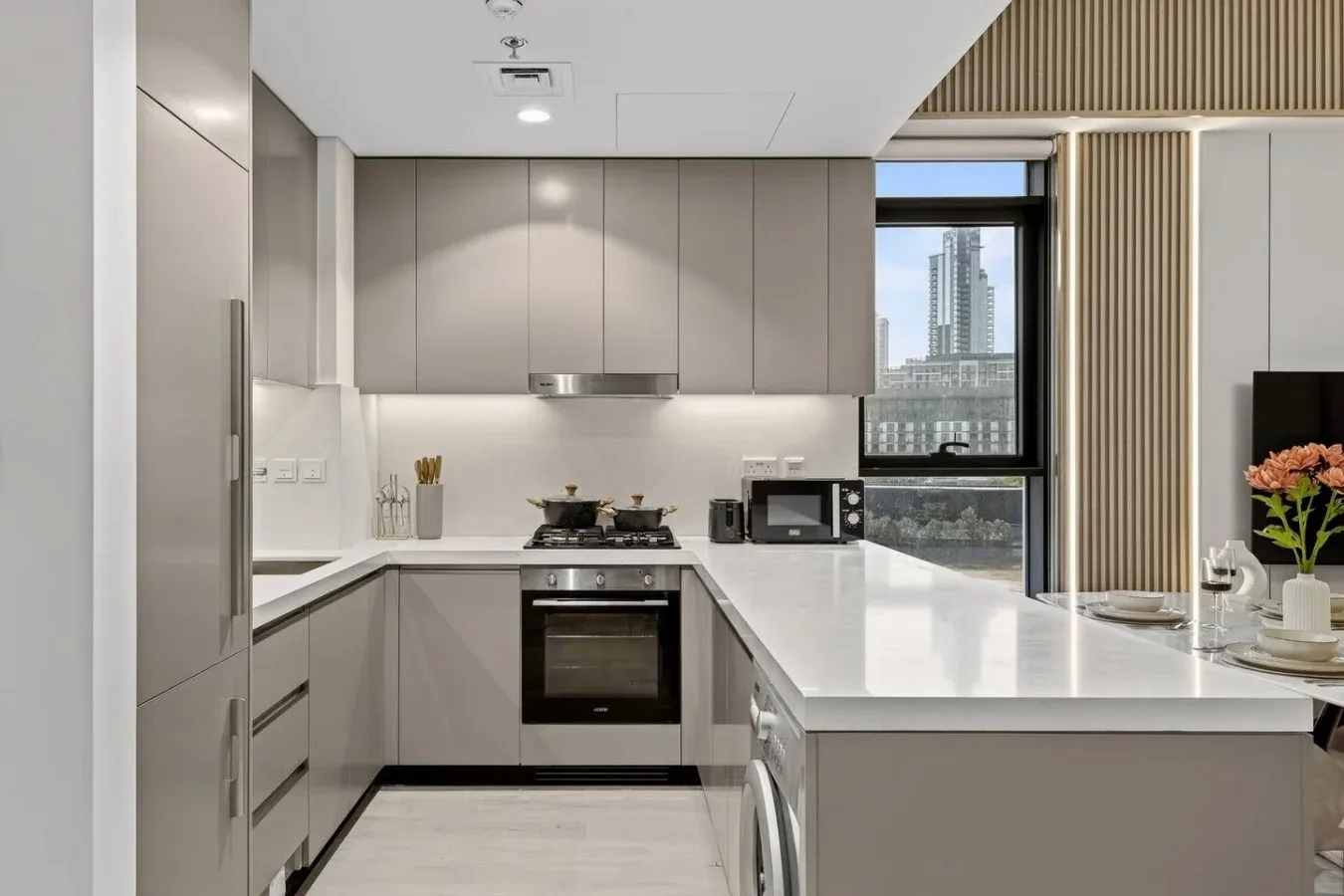 A modern kitchen with gray cabinetry, white counters, and a large window.