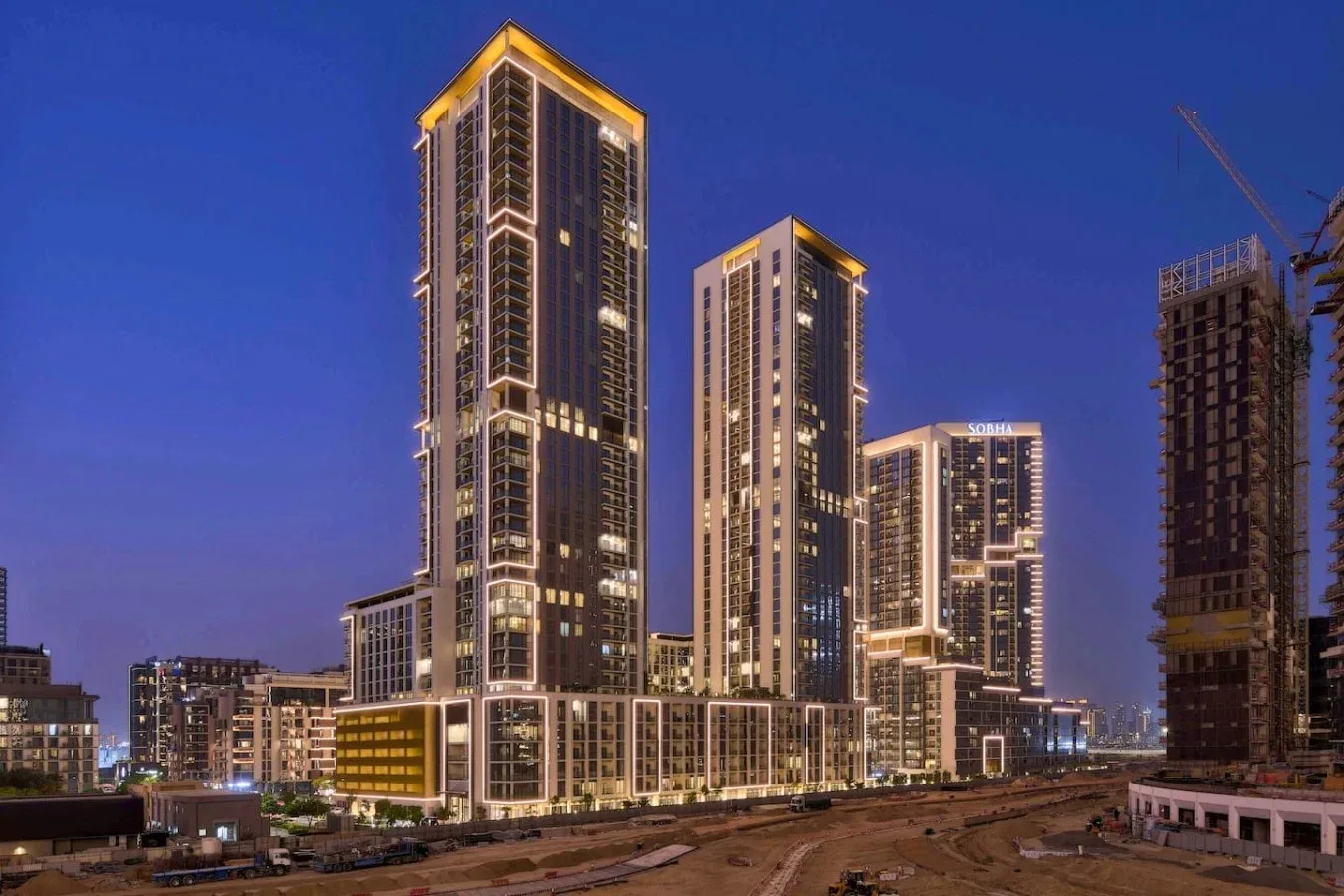 A city skyline at dusk, with illuminated high-rise buildings and a construction site.