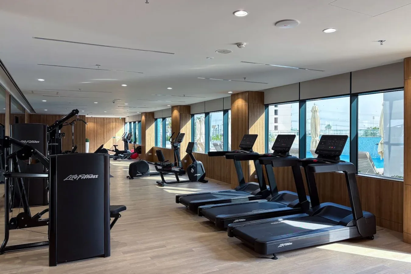 A gym with treadmills and exercise equipment beside large windows.