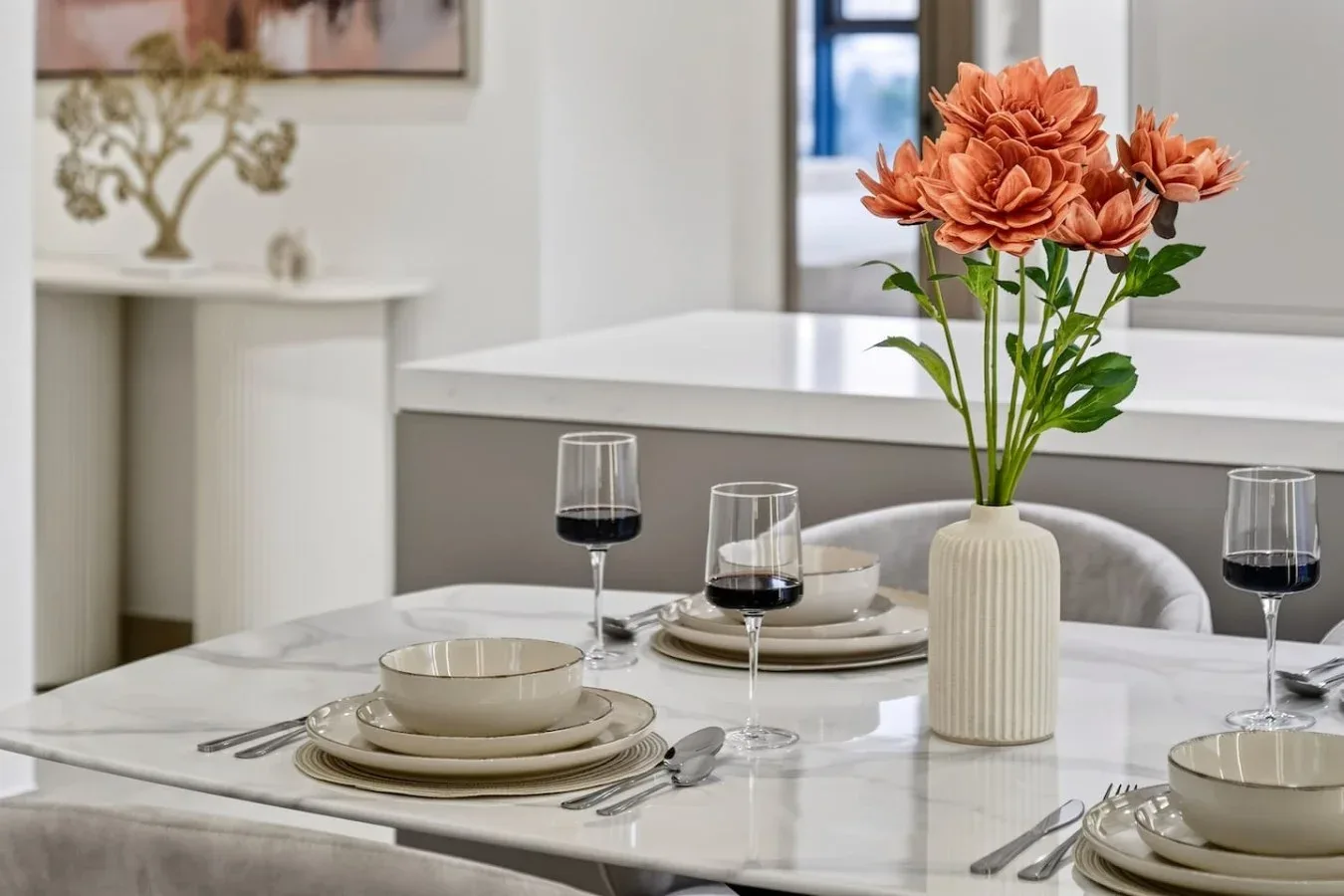A dining table set with dishes and a vase of orange flowers.