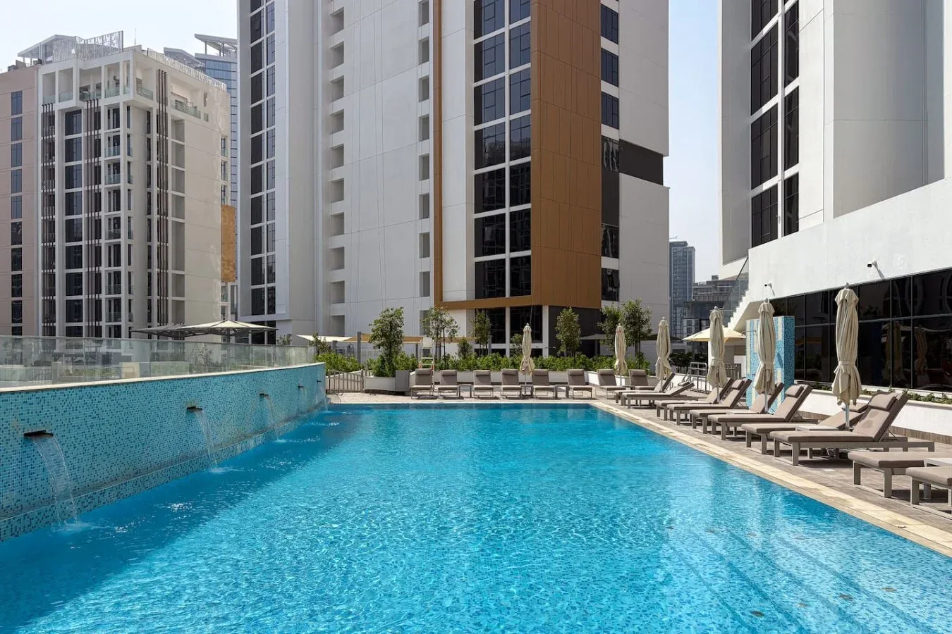 A rooftop swimming pool is surrounded by lounge seating and tall buildings.