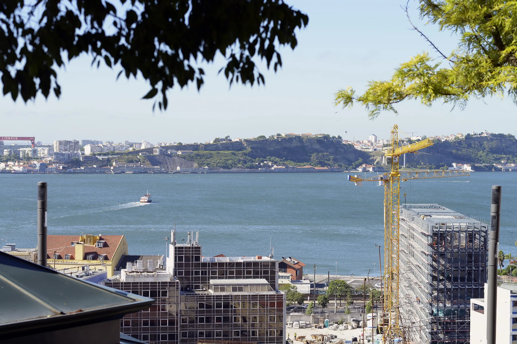 A broad river view with buildings and a construction crane in the foreground.