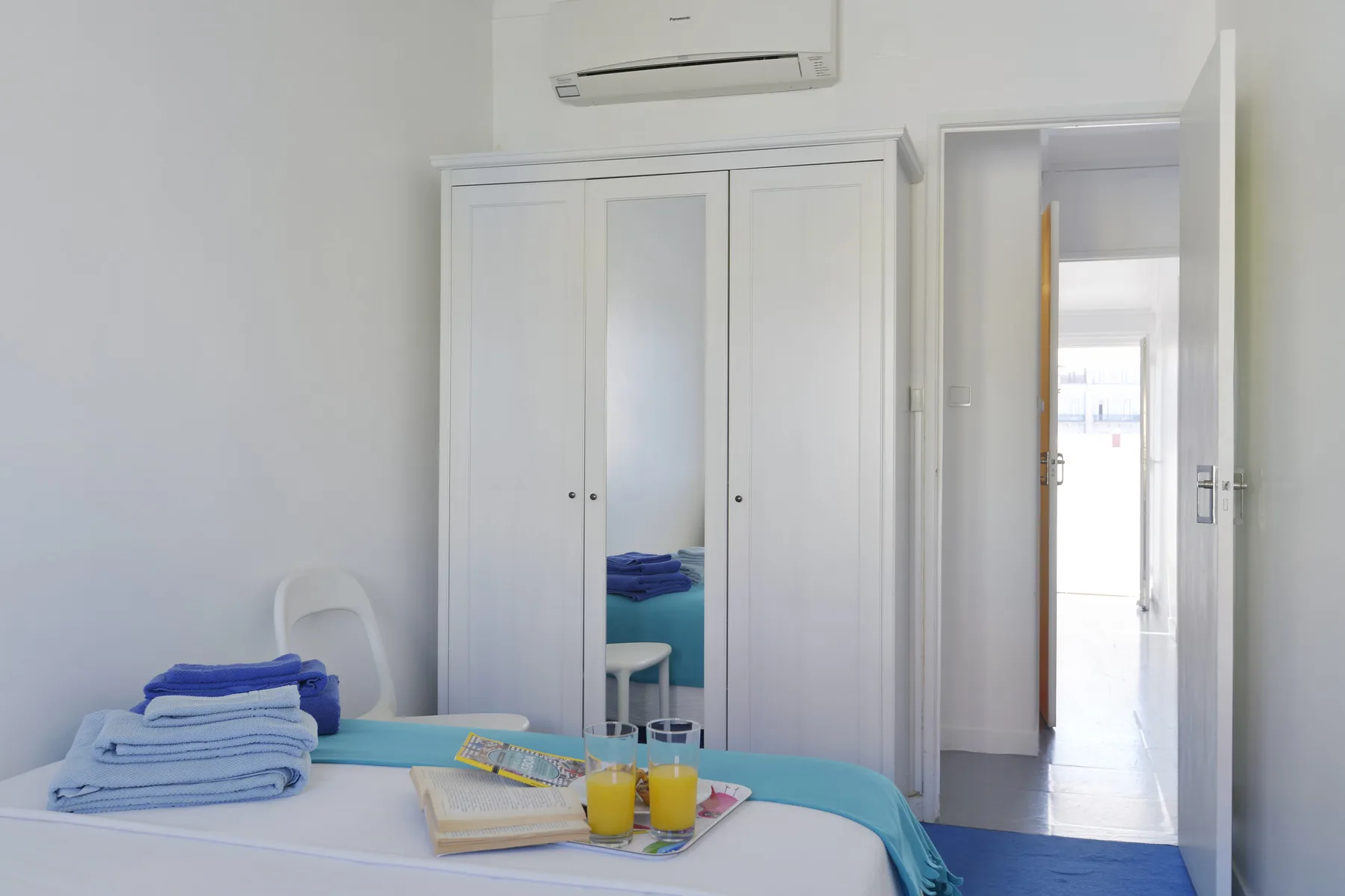 A bright bedroom with a bed, wardrobe, and an open doorway.