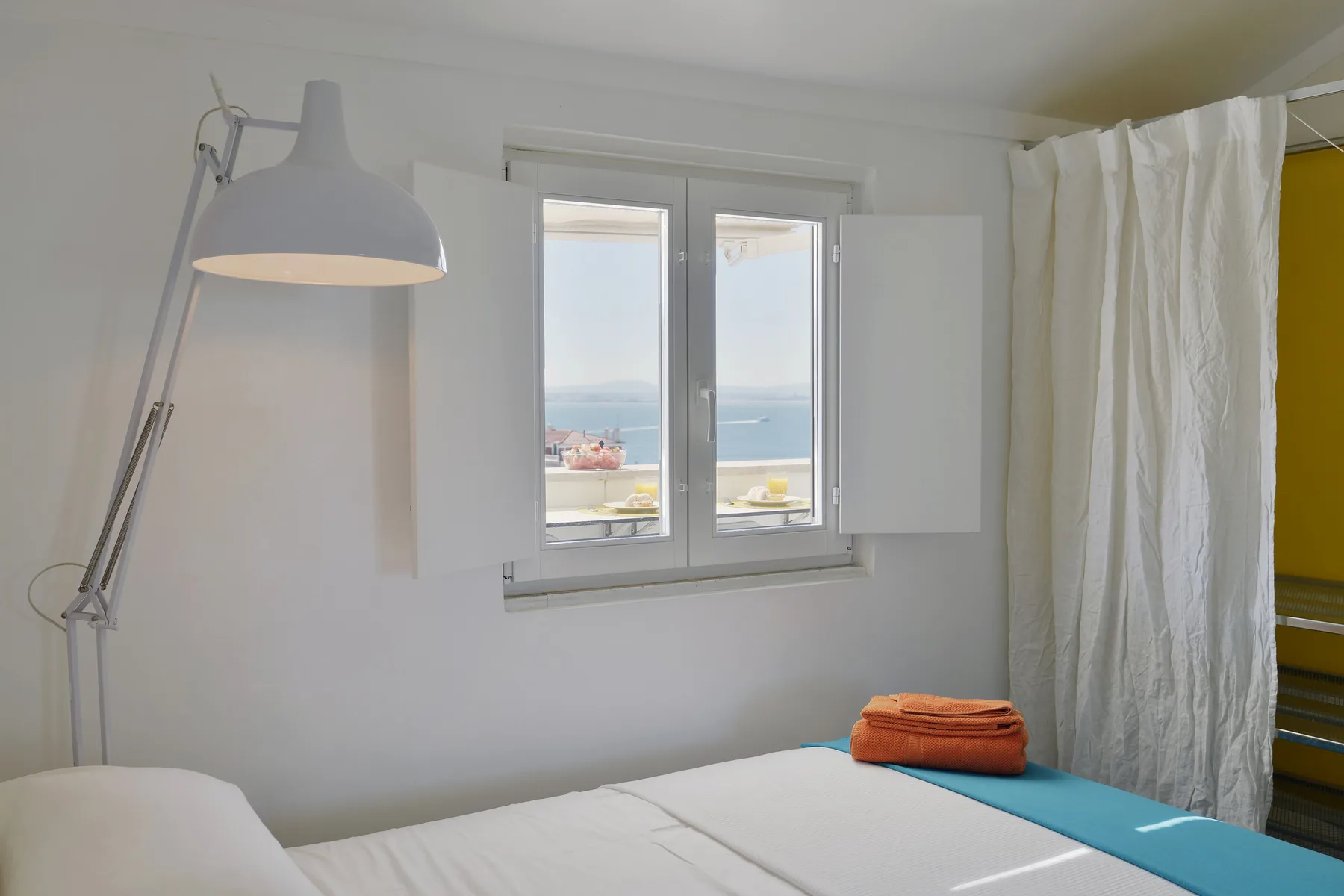 A bedroom with a window overlooking the water and a bed in the foreground.