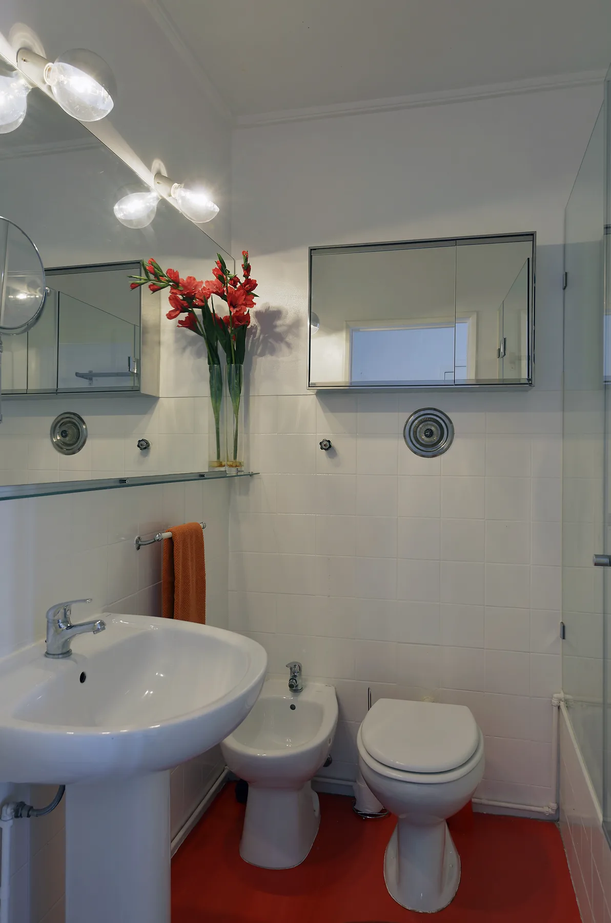 A tiled bathroom with a sink, toilet, and red floor.