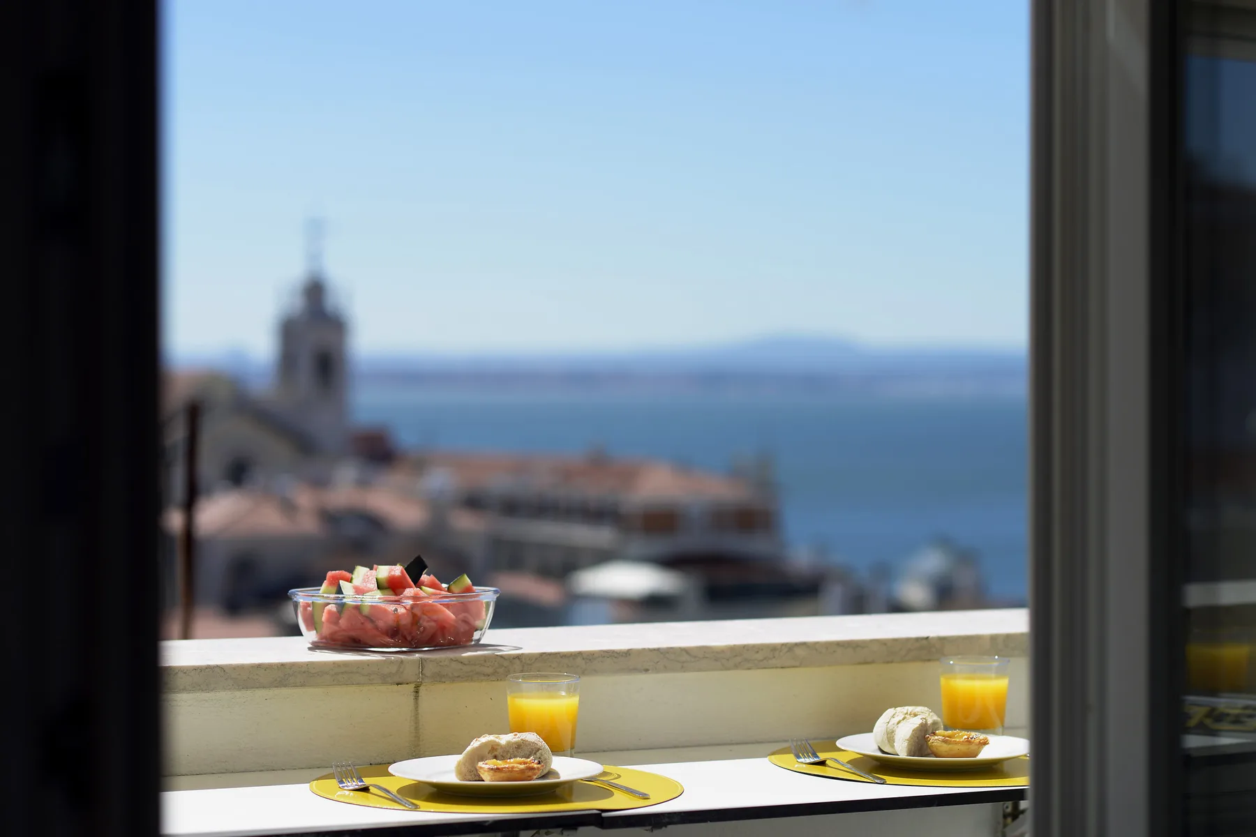 A breakfast table by an open window overlooks rooftops and the water.