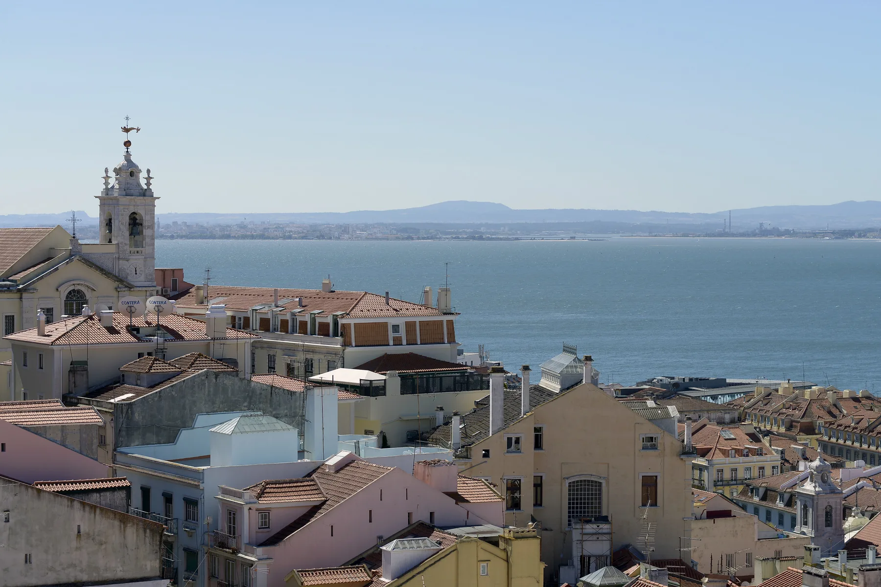 Rooftops of a coastal city overlook a broad expanse of water.