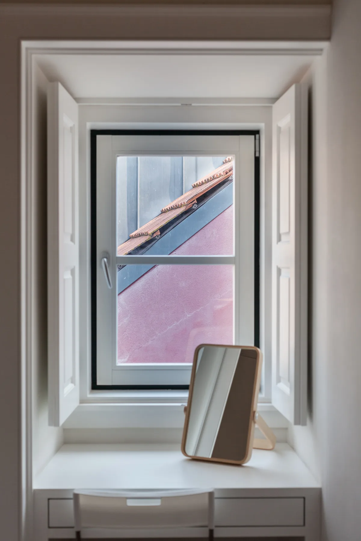 A bright room with a window overlooking nearby rooftops and a chair by the sill.