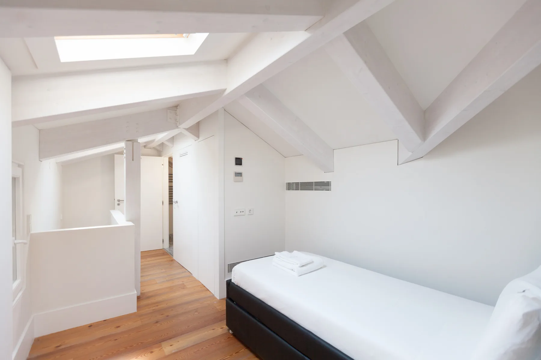 Un dormitorio luminoso con una cama bajo un techo inclinado y una claraboya.