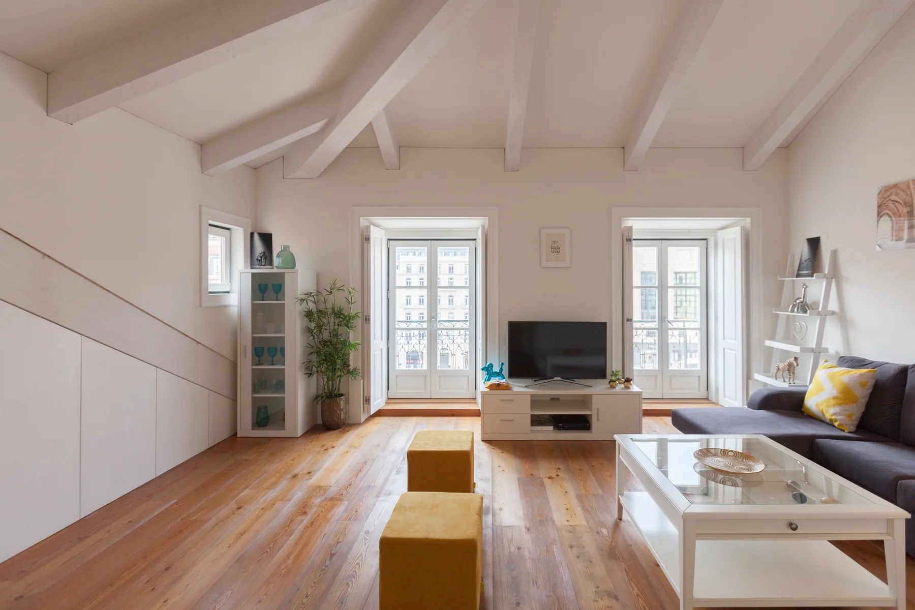 Una sala de estar luminosa con televisión, asientos y ventanas altas.