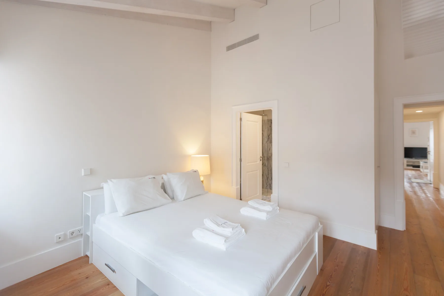 Un dormitorio luminoso con una cama blanca y suelo de madera.