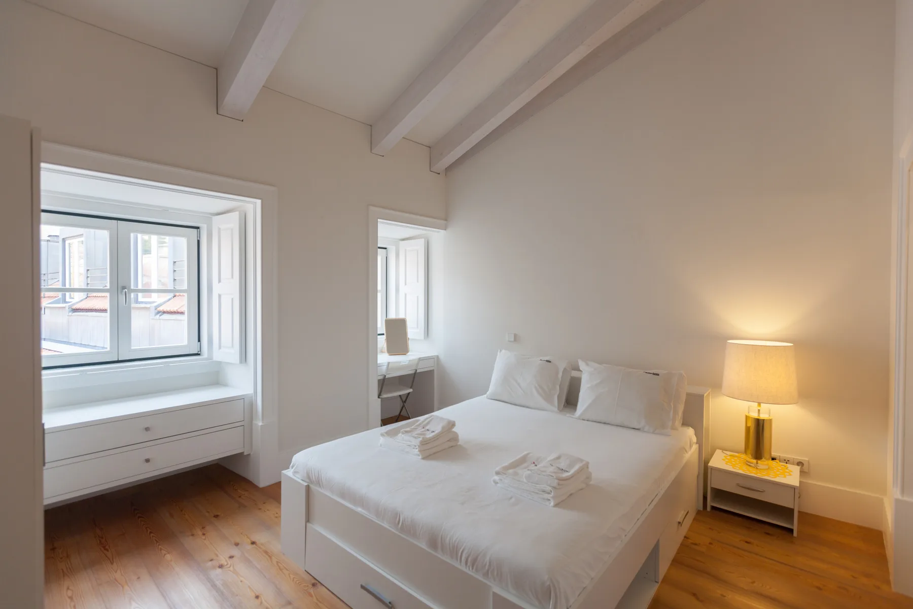Un dormitorio luminoso con una cama, una lámpara de noche y ventanas grandes.