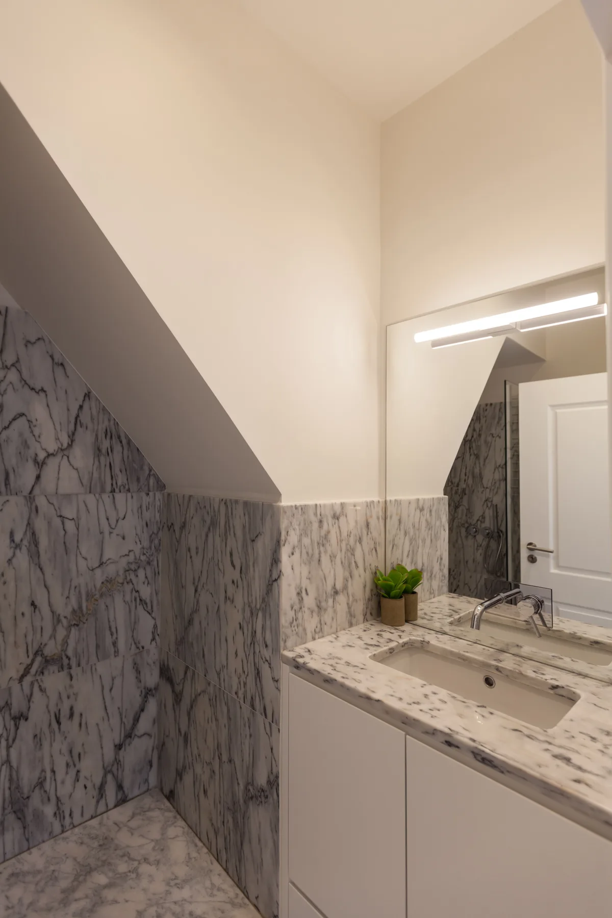 Un lavabo de baño con espejo bajo un techo inclinado.