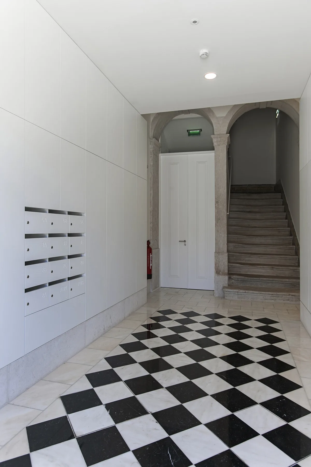 Un pasillo con suelo de baldosas, una puerta blanca y escaleras.