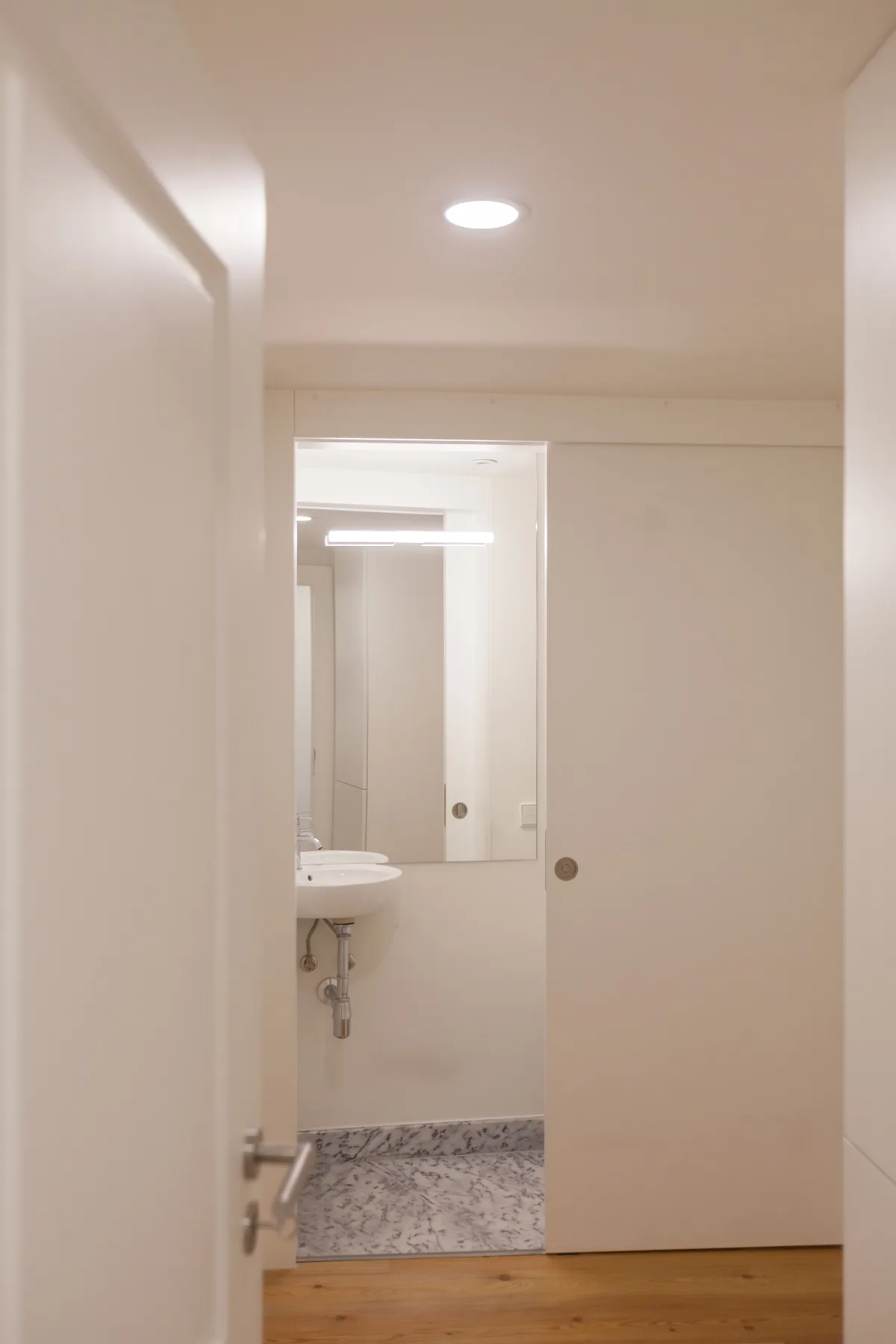 Un baño con lavabo y espejo se ve a través de una puerta parcialmente abierta.