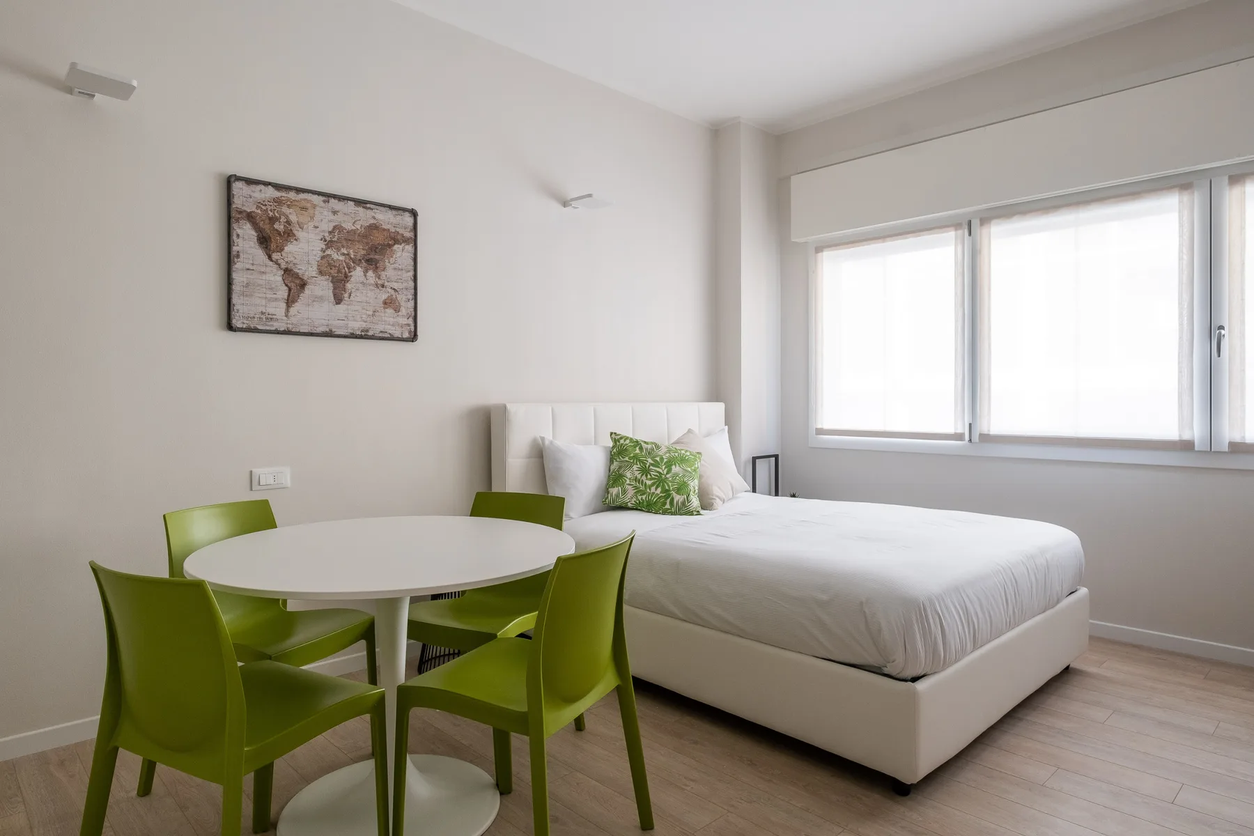 Un dormitorio luminoso con una cama y una pequeña mesa de comedor con asientos verdes.