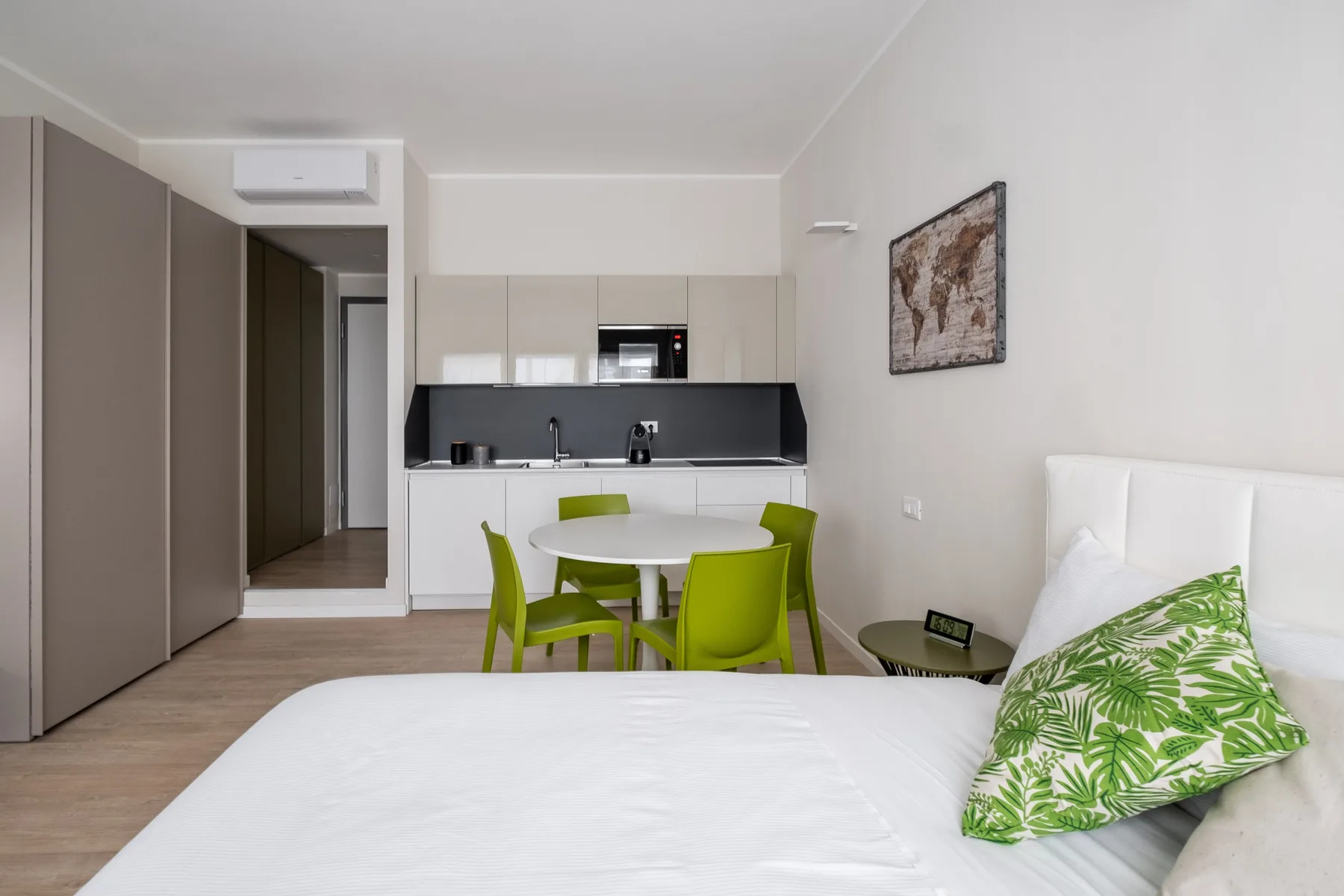Un dormitorio luminoso con una cama blanca y un pequeño comedor junto a una cocina.