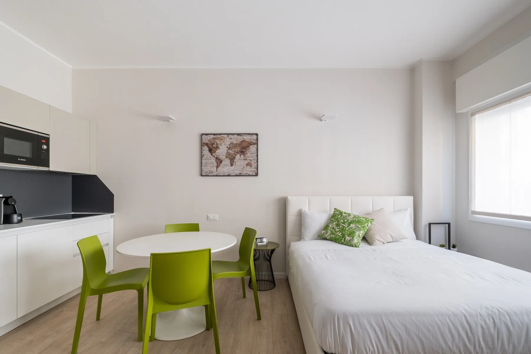 Un dormitorio luminoso con una cama, una mesa pequeña y asientos verdes.