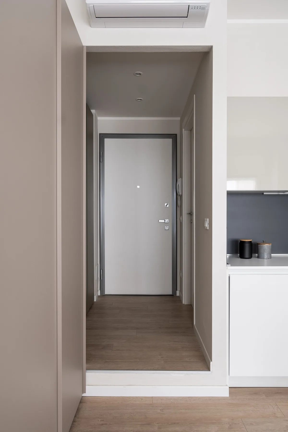 Un pasillo de entrada estrecho conduce a una puerta cerrada, con parte de una cocina a un lado.