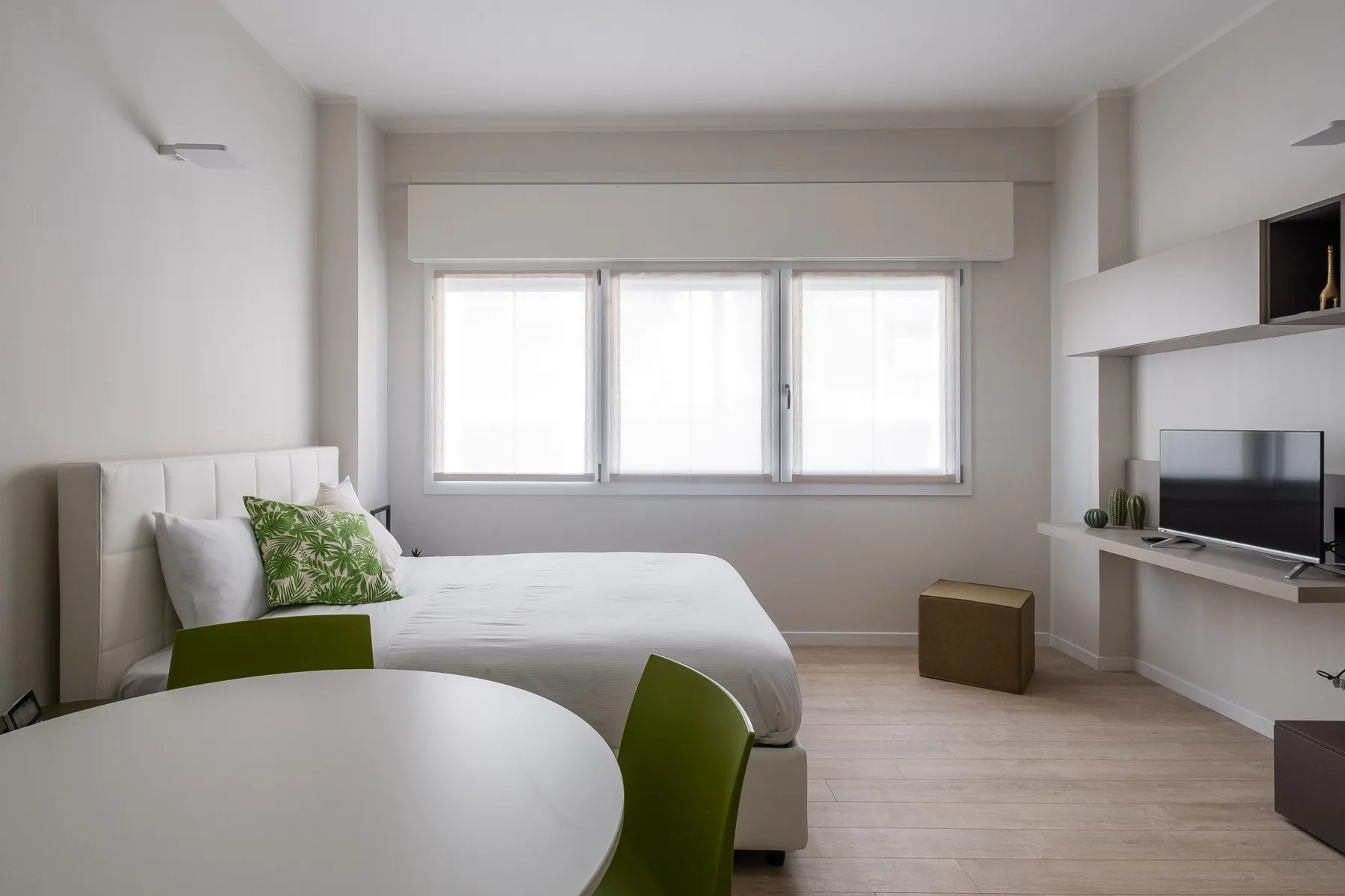Un dormitorio luminoso con una cama, una mesa redonda y un televisor.