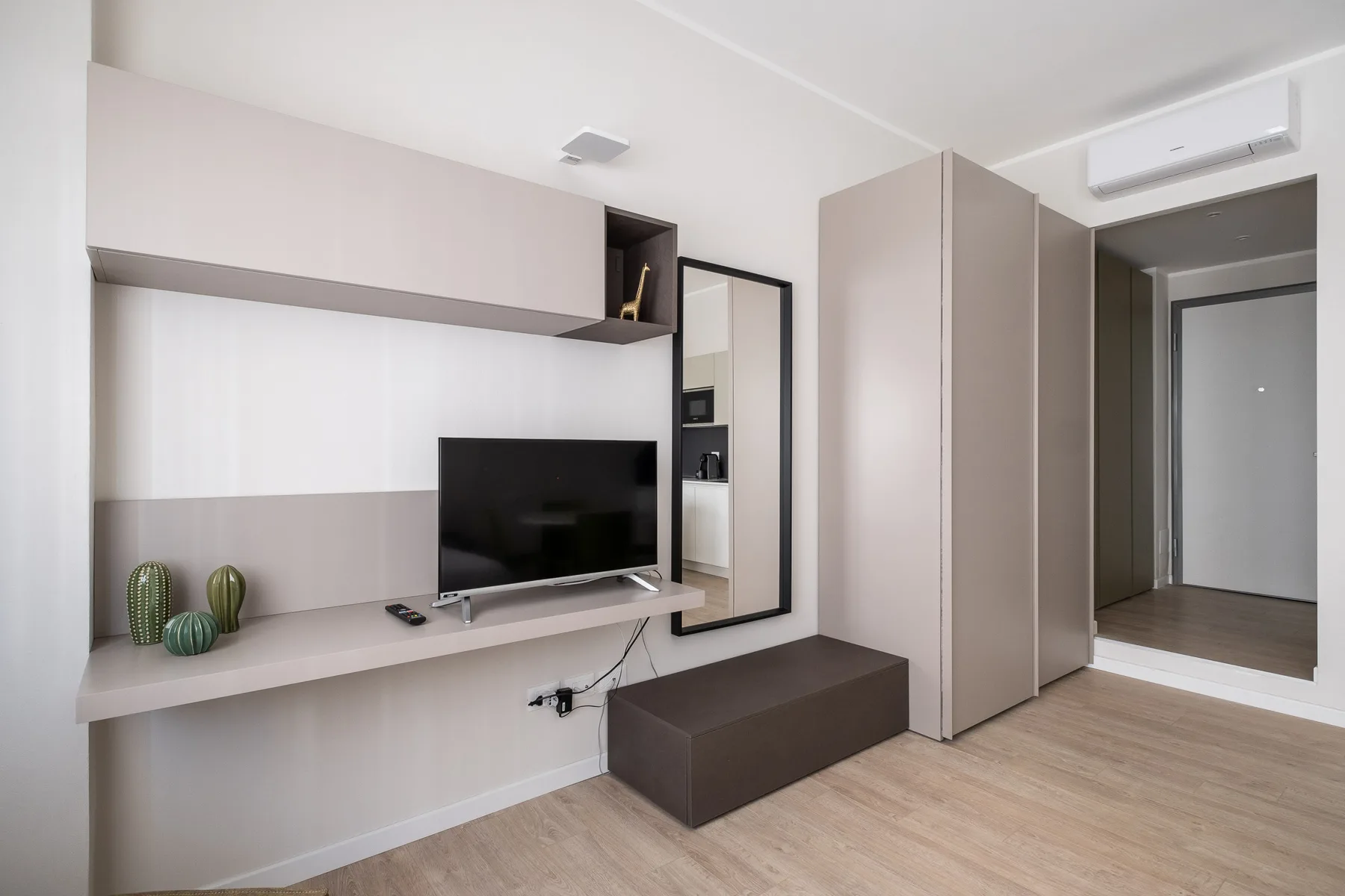 Una pared de dormitorio con televisor, estantes flotantes y un banco bajo.