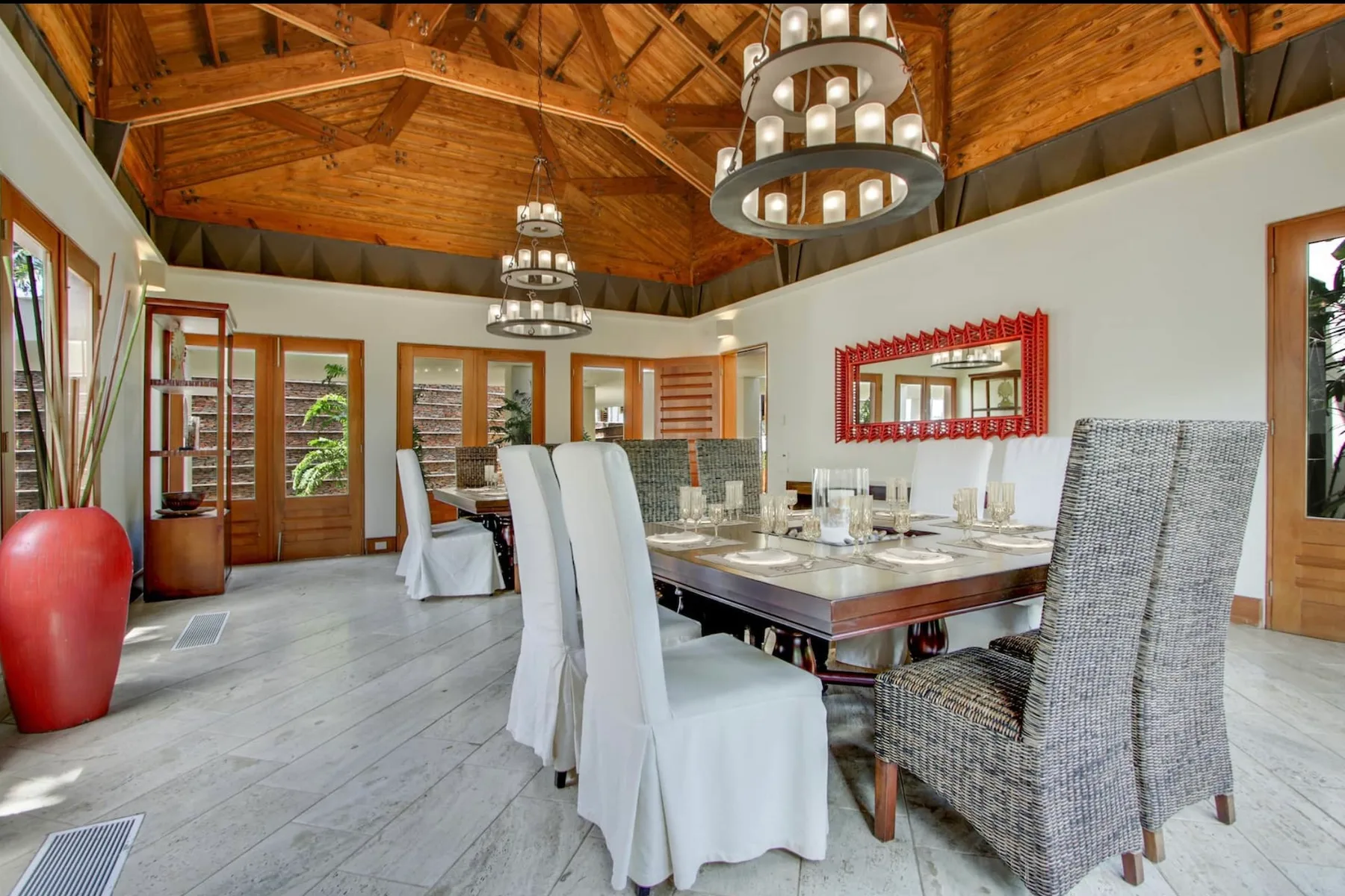 A dining room with a long table and chairs beneath a timber ceiling.