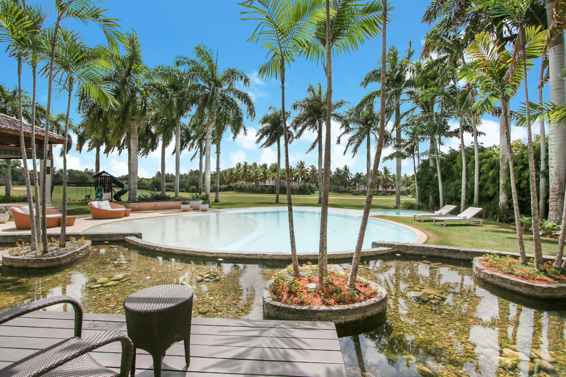 An outdoor pool is surrounded by palm trees and landscaped gardens.