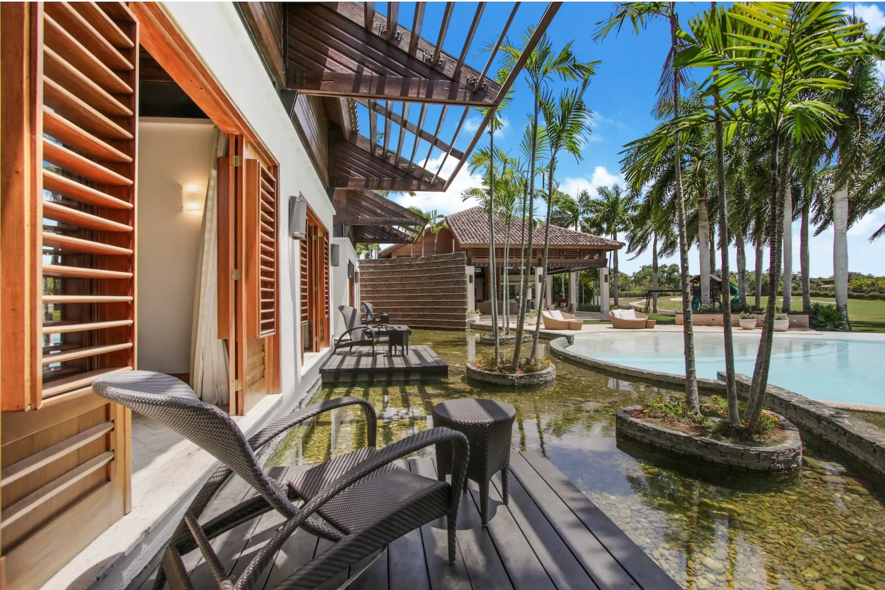 An outdoor seating area beside a pool, with palm trees and wooden decking.