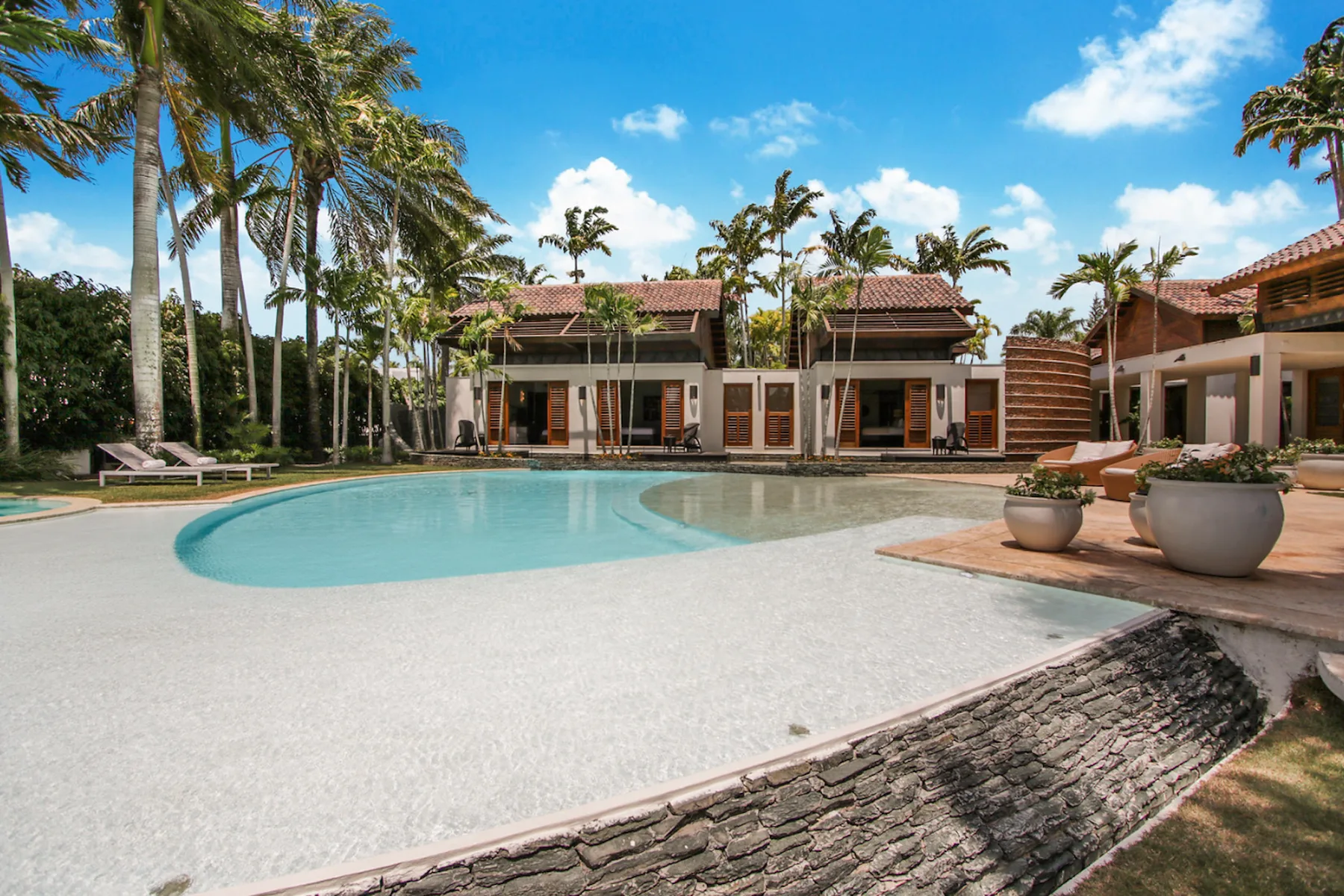 A resort-style pool sits in front of a low-rise building with palm trees.