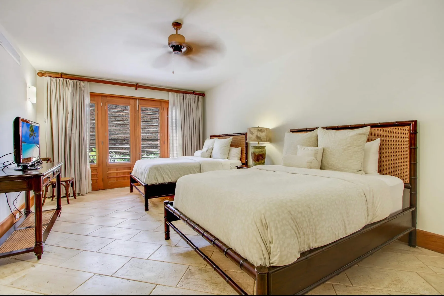 A bedroom with two beds, pale bedding, and wood-framed doors opening to a balcony.