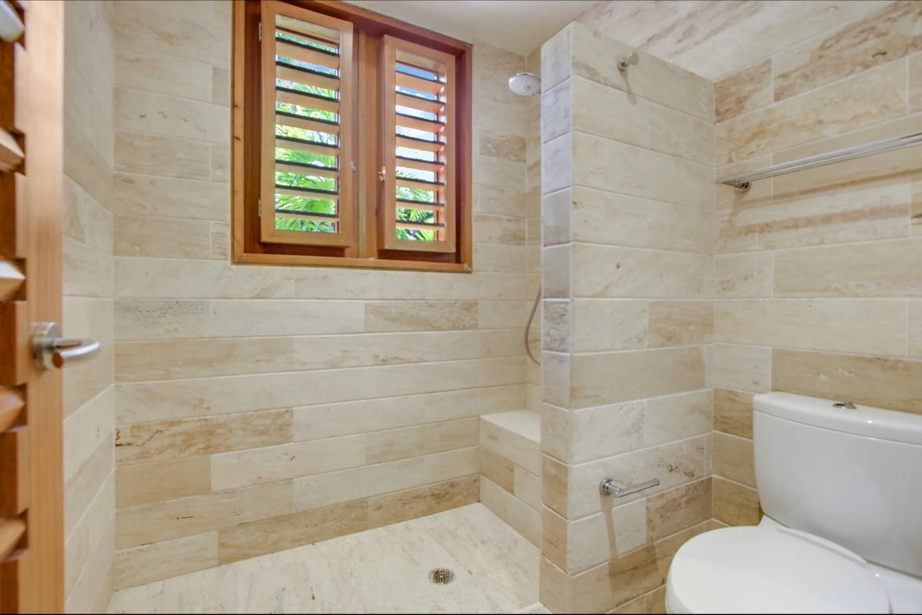 A tiled bathroom with a shower area, louvered window, and toilet.