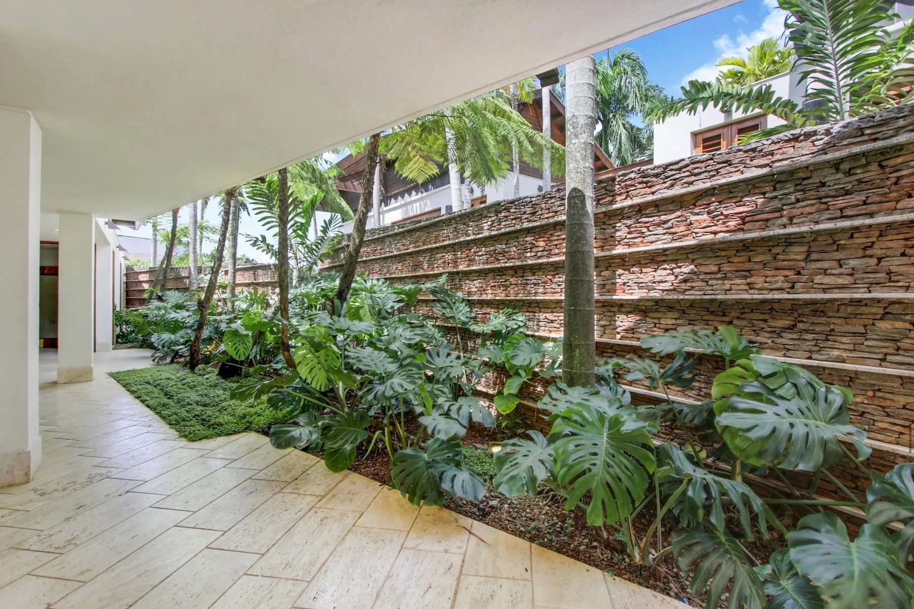 A covered outdoor walkway borders a planted garden and layered stone wall.