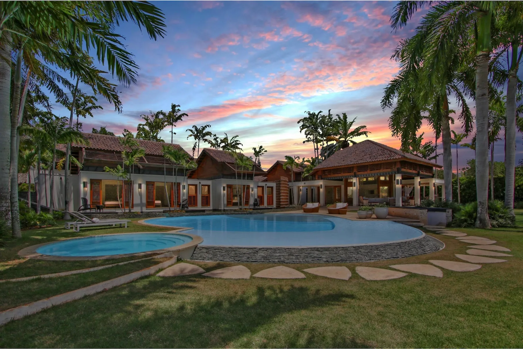 A tropical resort-style courtyard with a swimming pool beneath a colorful sunset sky.
