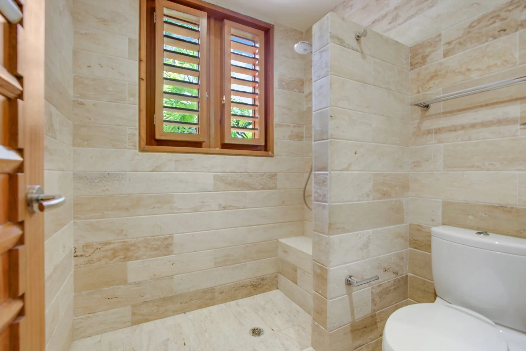 A tiled bathroom with a louvered window and a toilet.