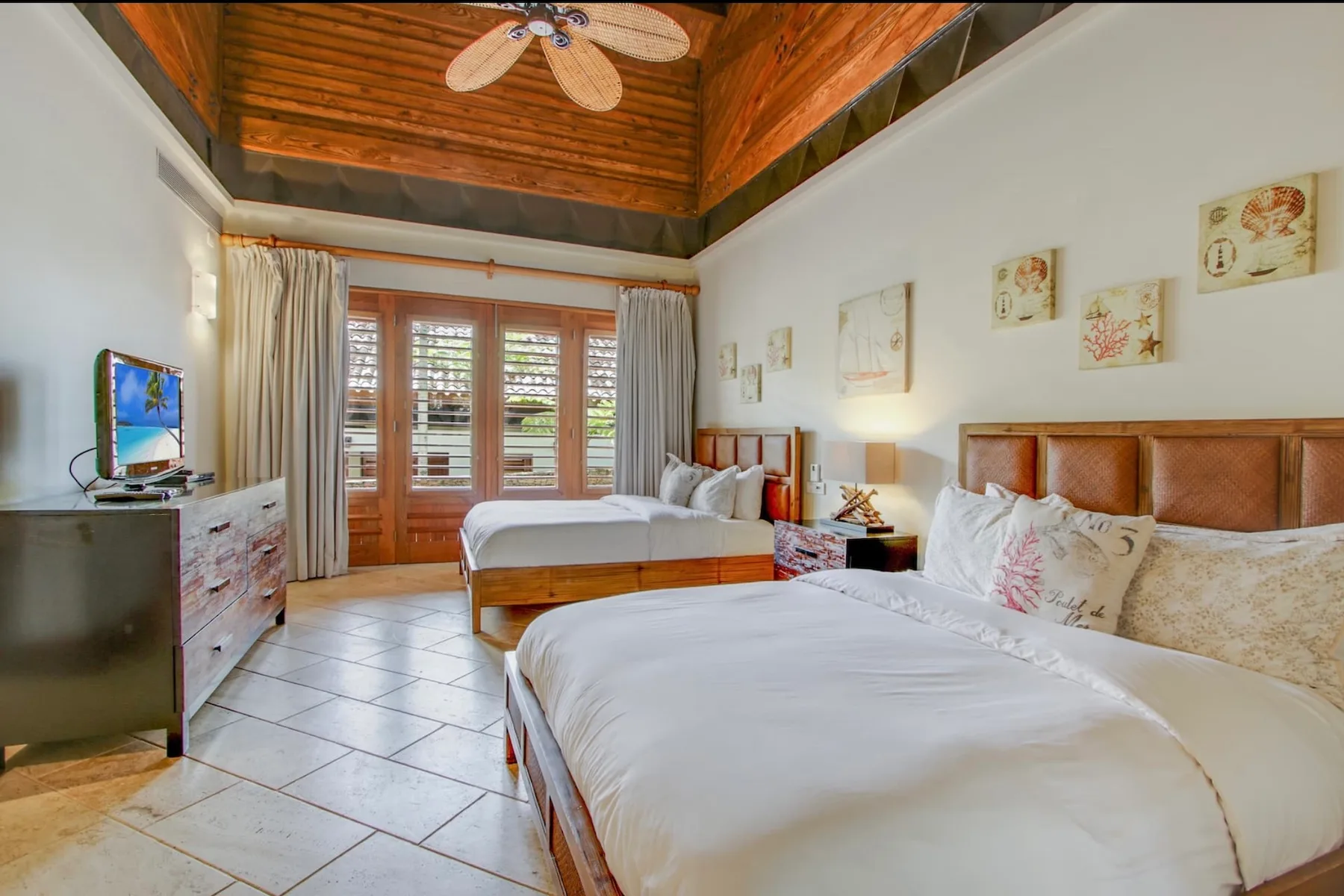 A bright bedroom with two beds and wooden doors opening to a balcony.
