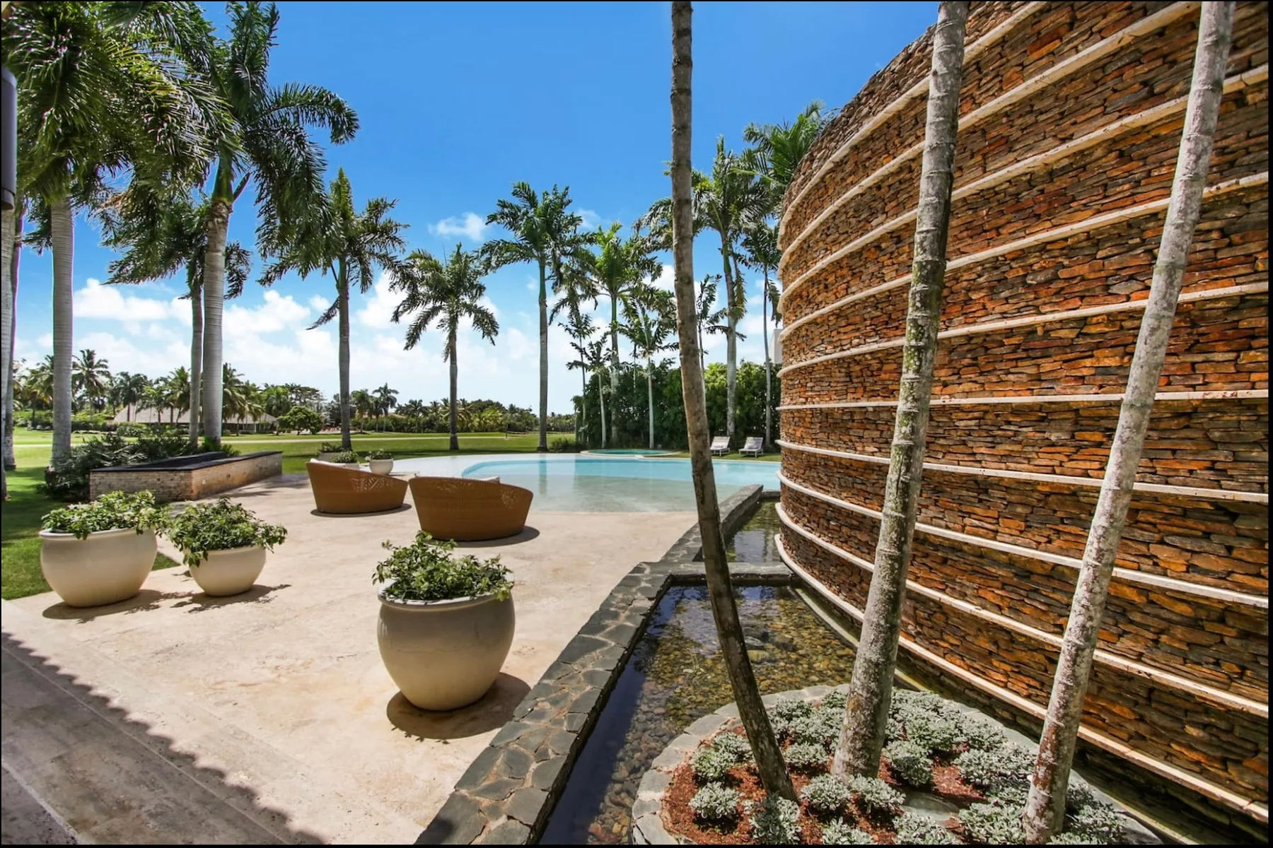 A landscaped poolside courtyard with palm trees, planters, and a curved stone wall.