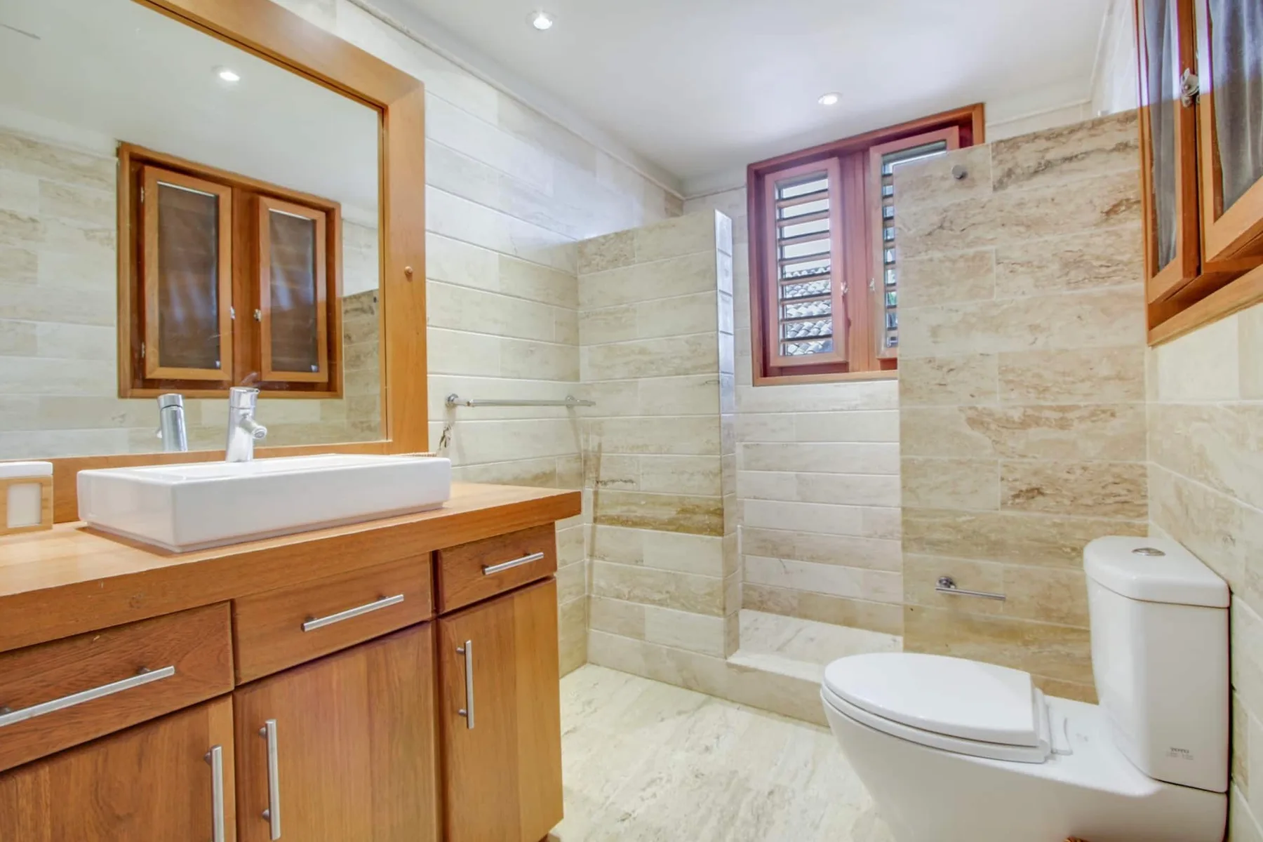 A tiled bathroom with a wooden vanity, sink, and toilet.