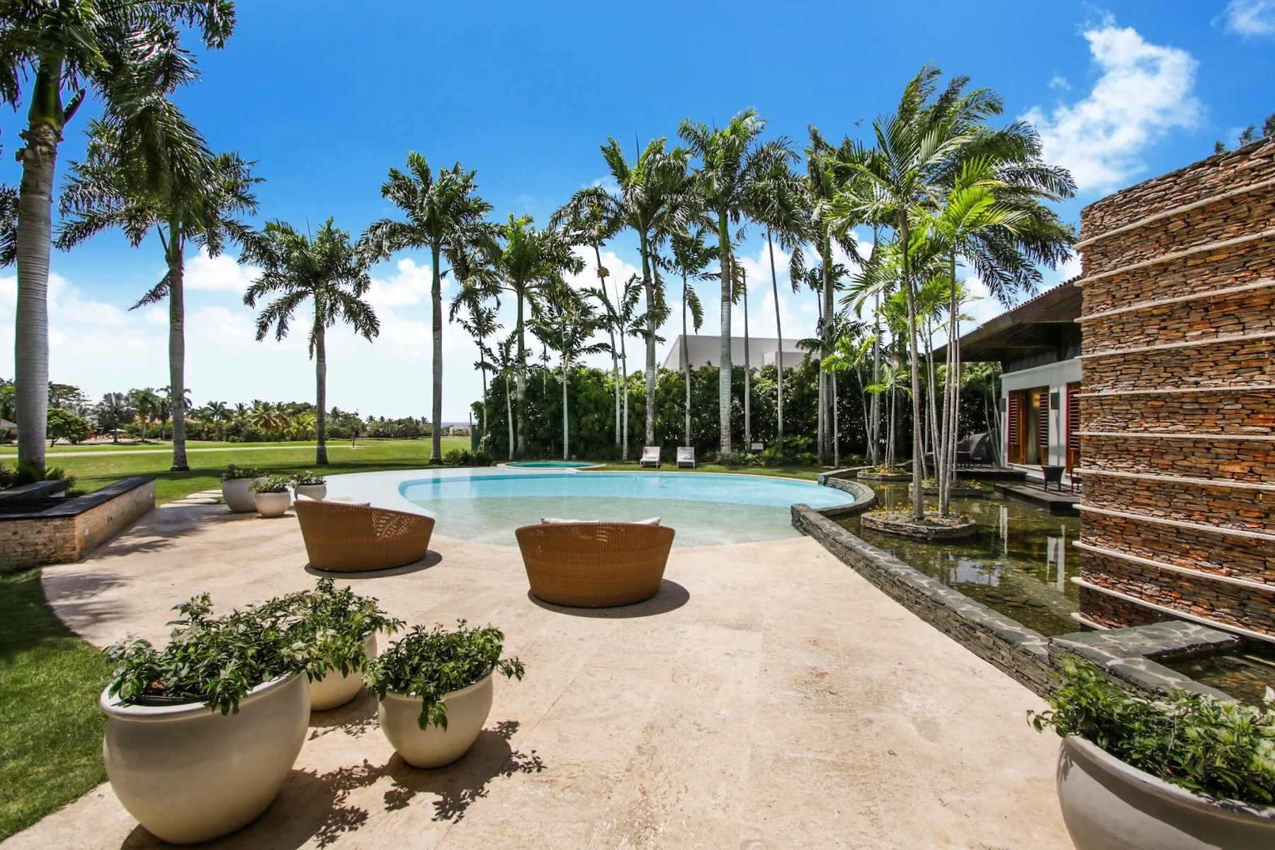 A landscaped outdoor pool area with palm trees, seating, and a modern building.