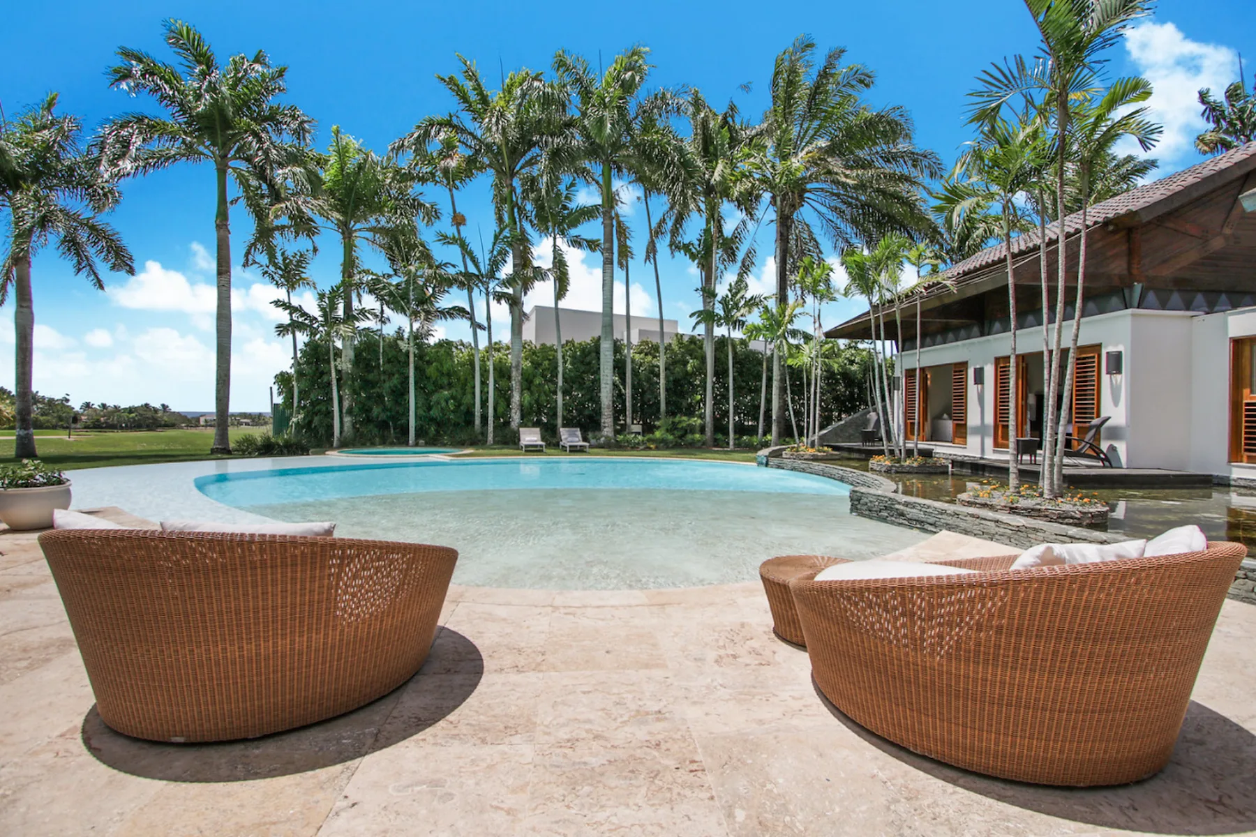 A curved outdoor swimming pool beside a building, with seating on the paved deck.