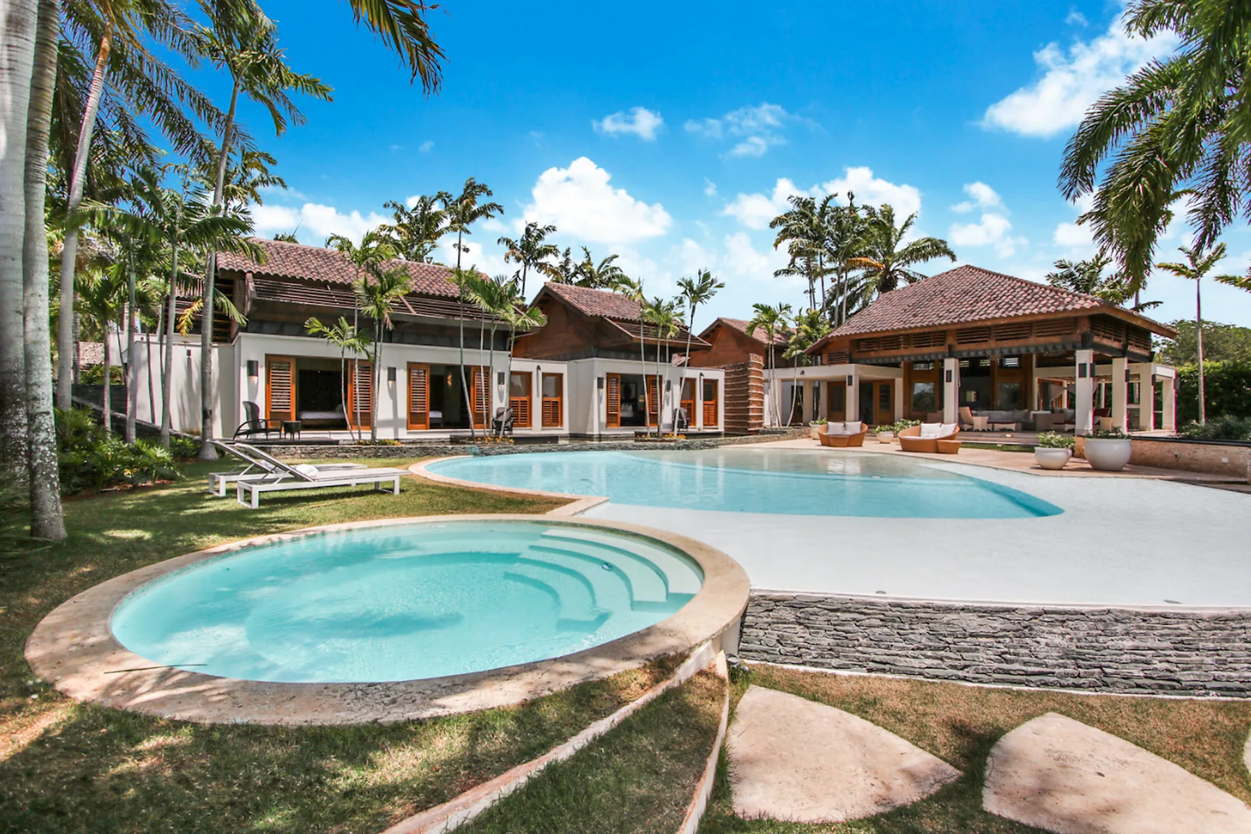 A tropical resort pool sits in front of low buildings and palm trees.