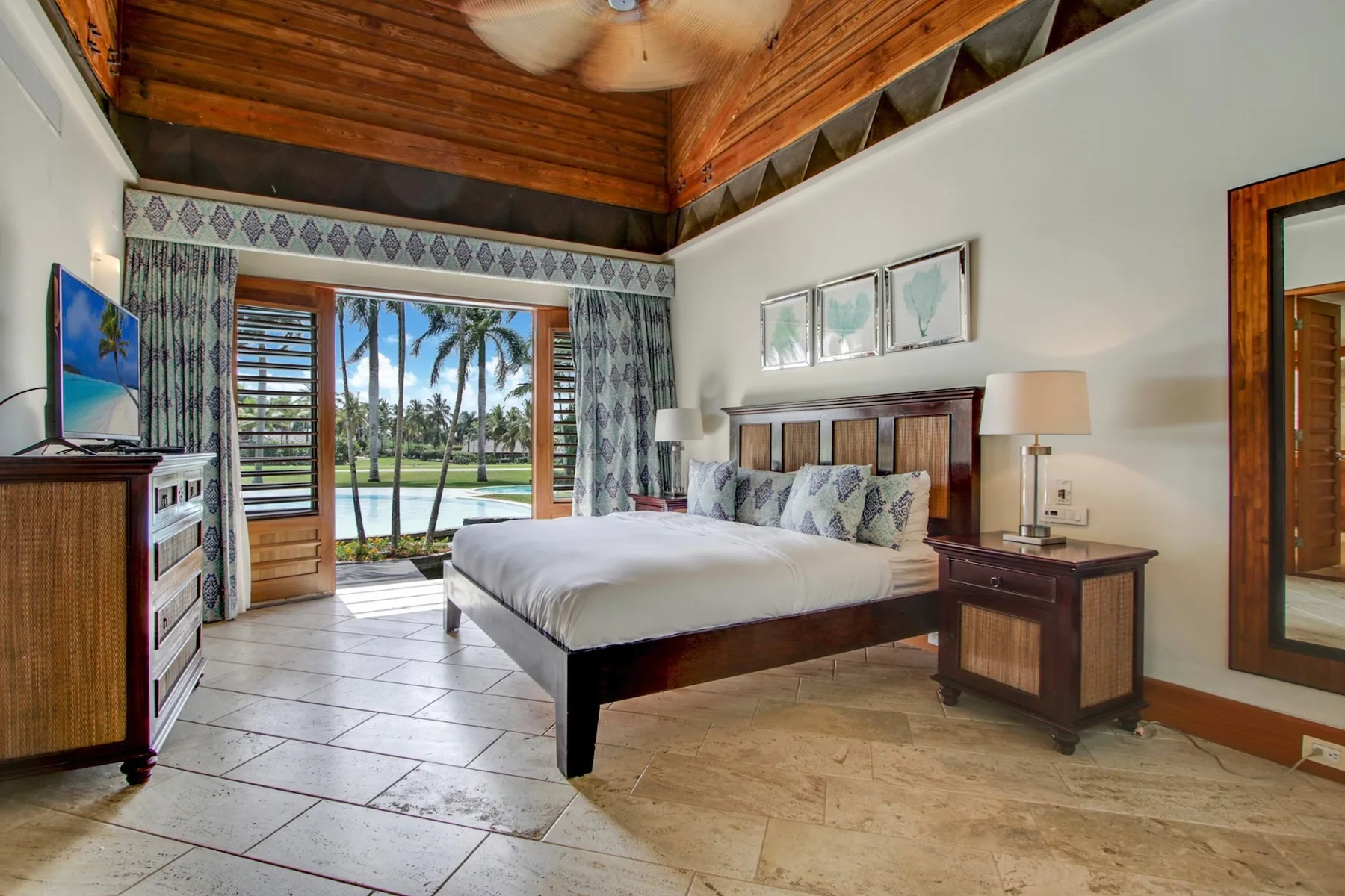 A bedroom with a large bed, wooden ceiling, and glass doors opening to a garden.
