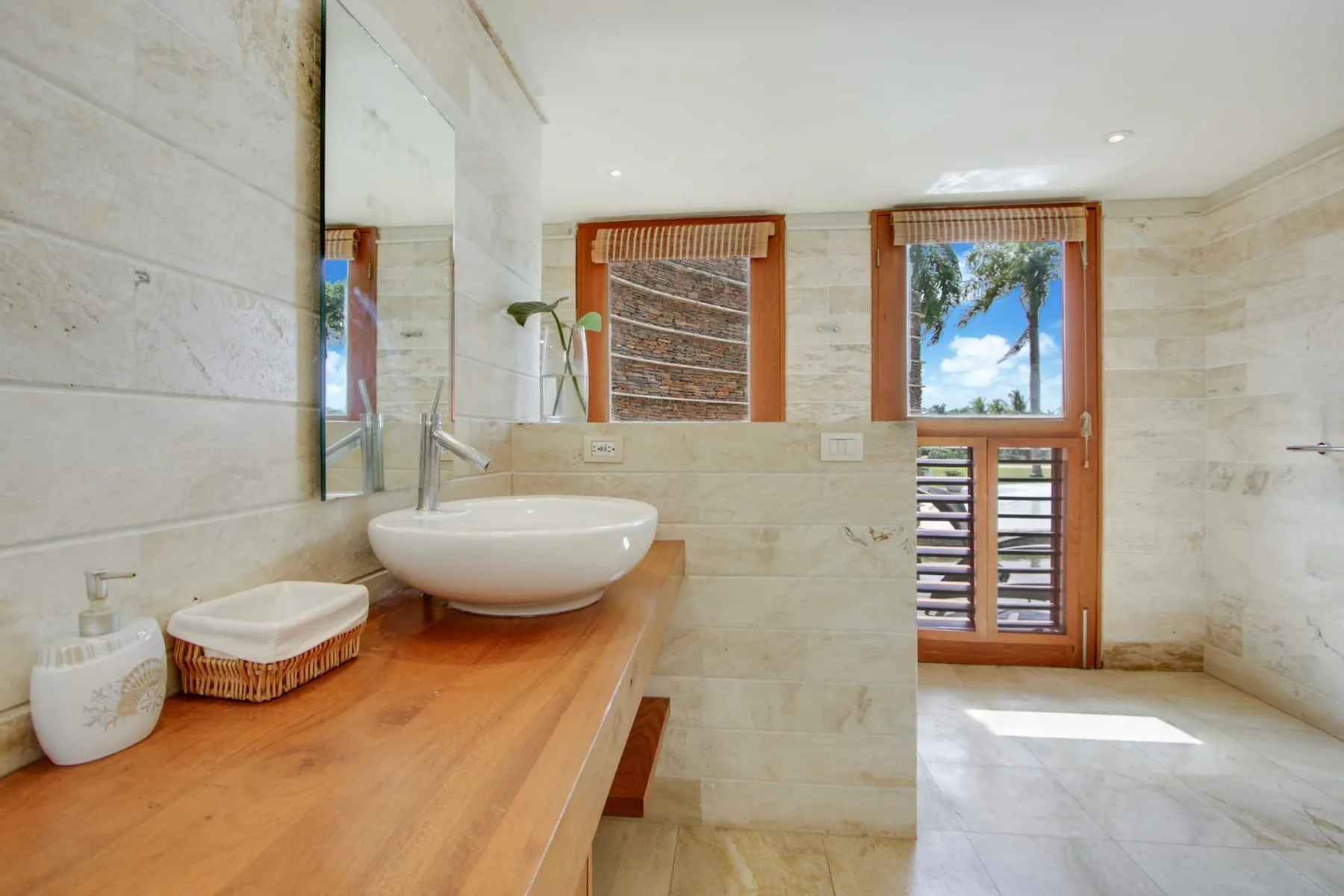 A bathroom with a vessel sink on a wooden vanity and a window overlooking greenery.