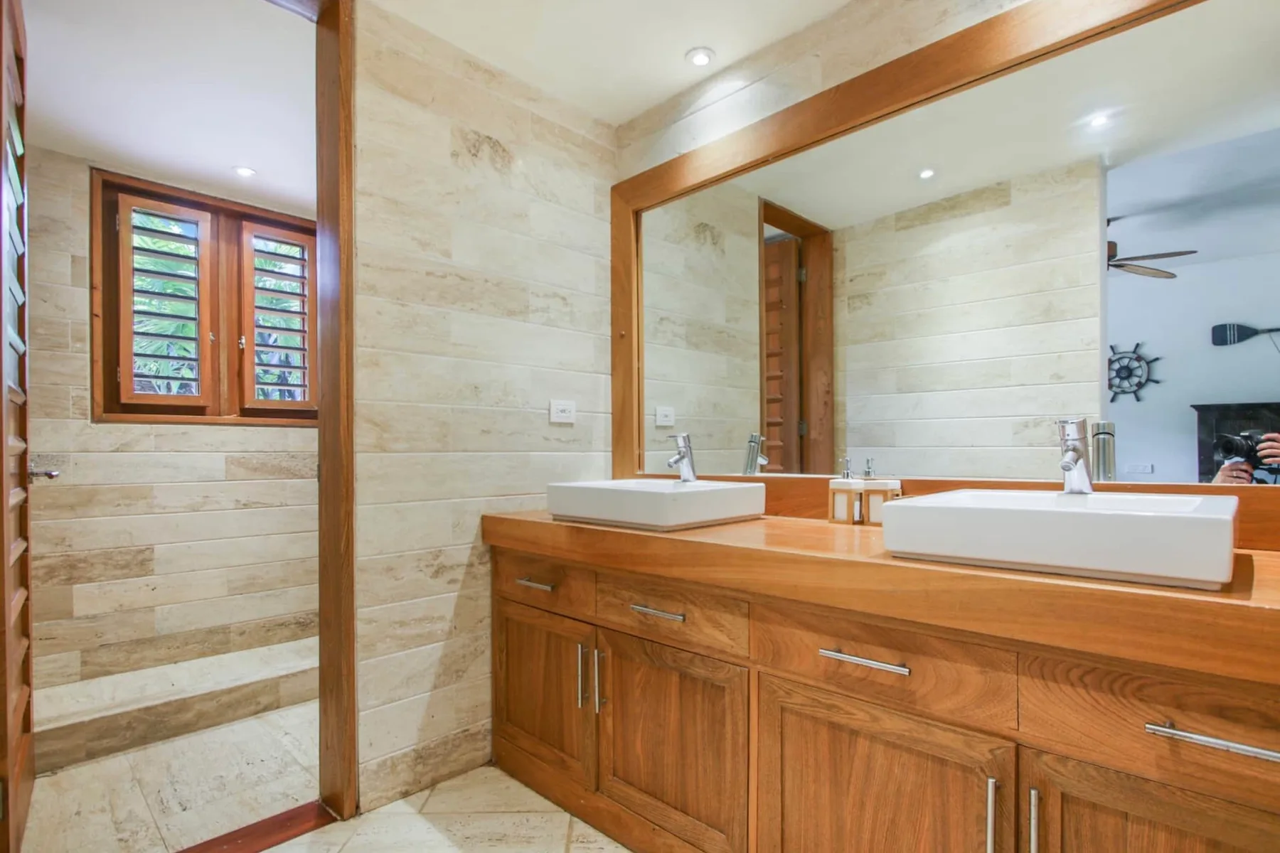 A tiled bathroom with a long wooden vanity and a large mirror.