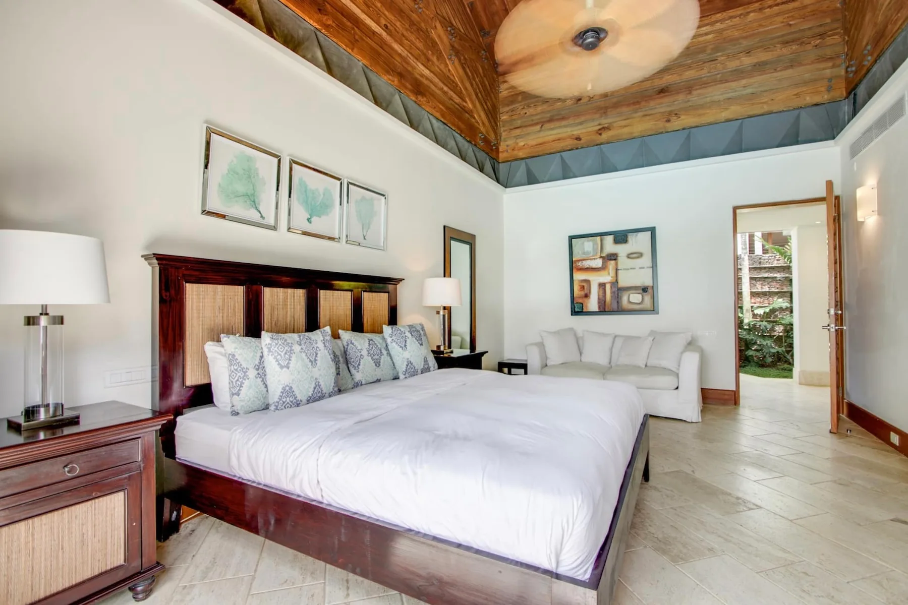 A bedroom with a large bed, framed artwork, and a sitting area.