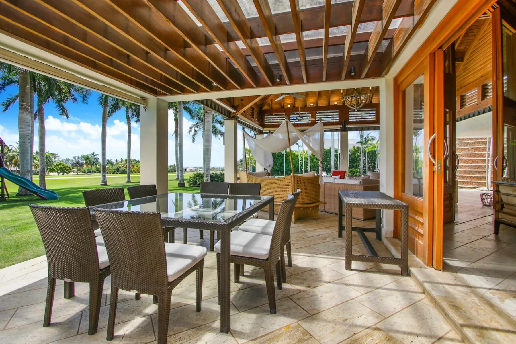 A covered patio dining area with tables and seating overlooks a grassy garden.