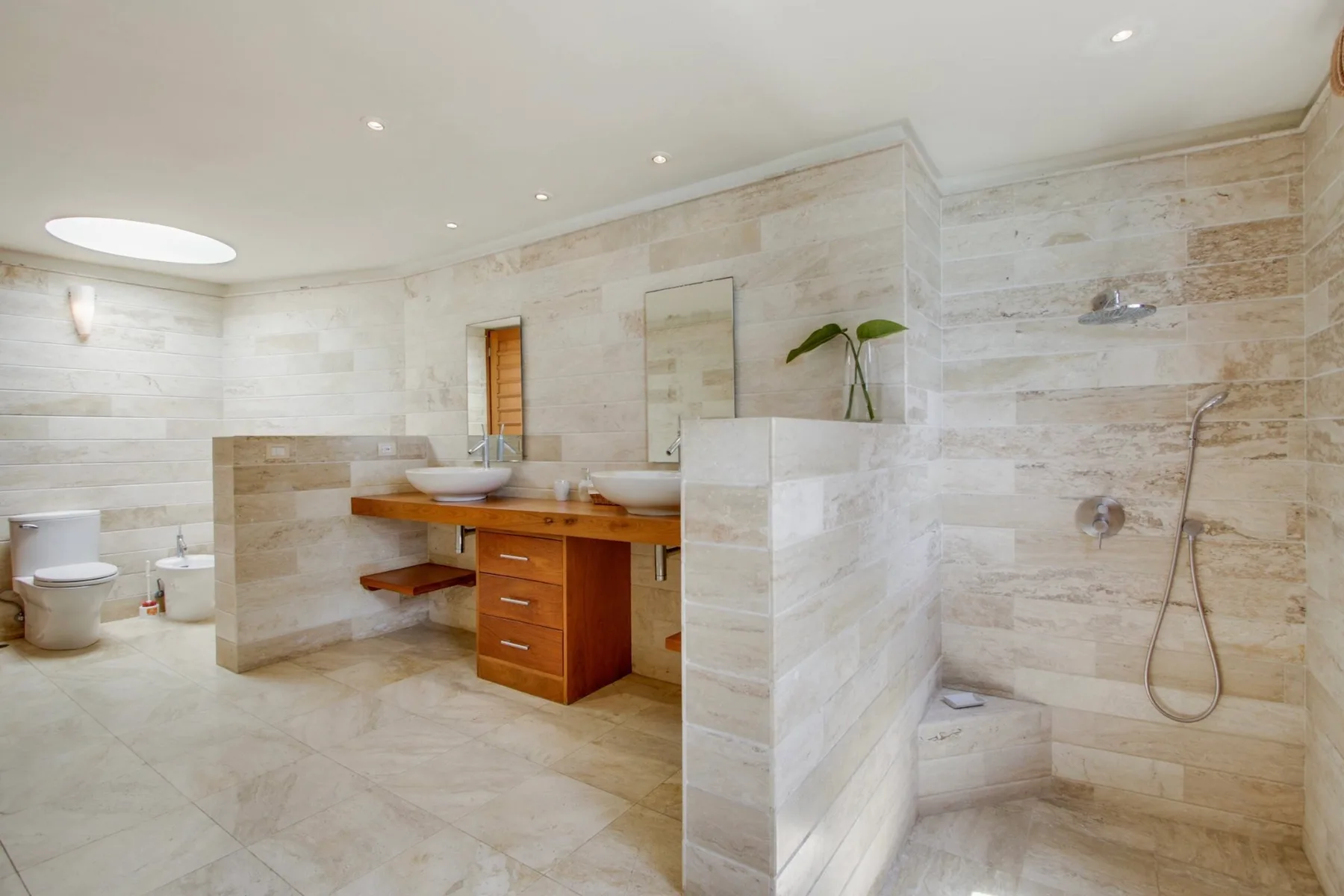 A spacious tiled bathroom with a vanity, toilet, and open shower area.
