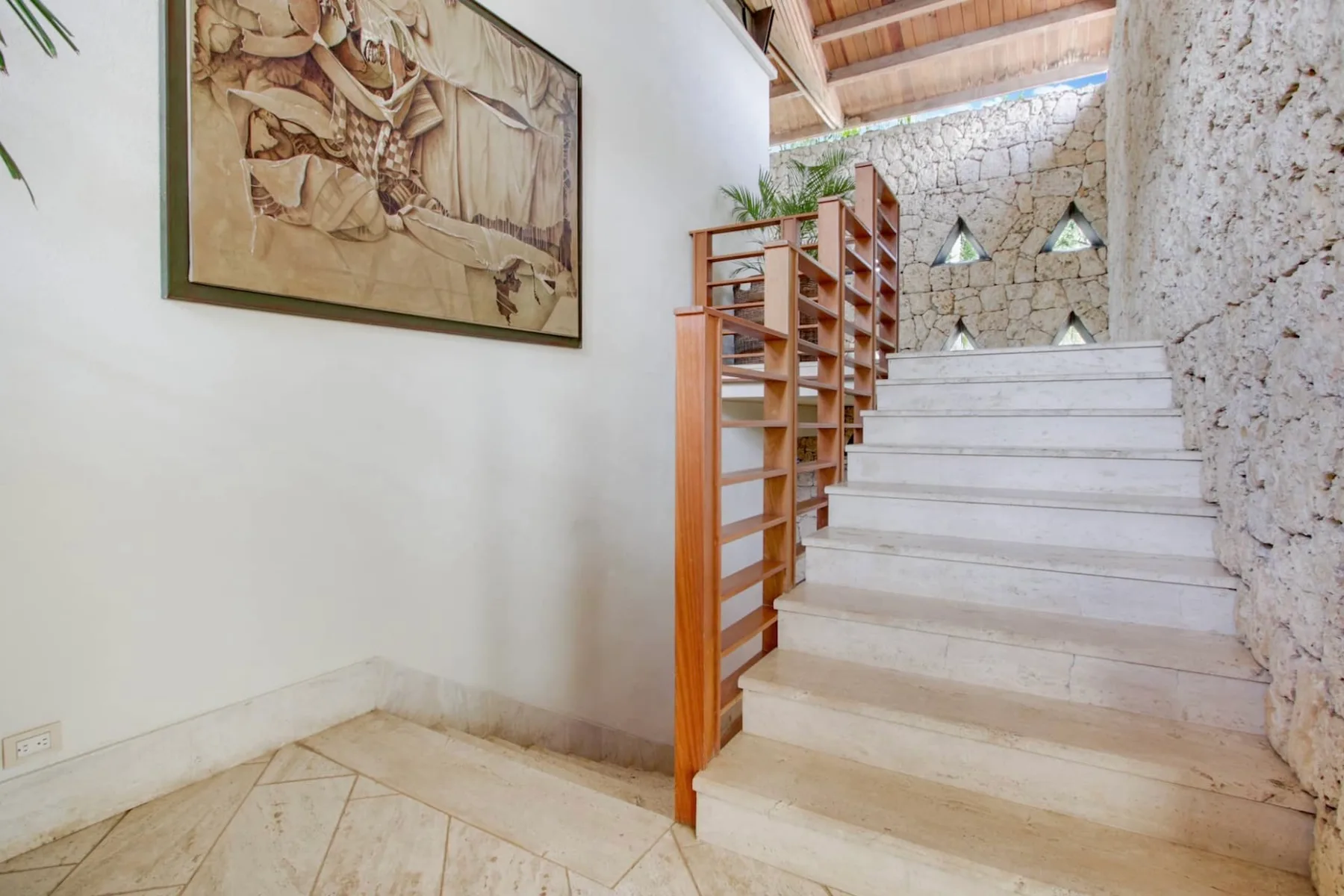A stone staircase rises beside a wooden railing and framed artwork.